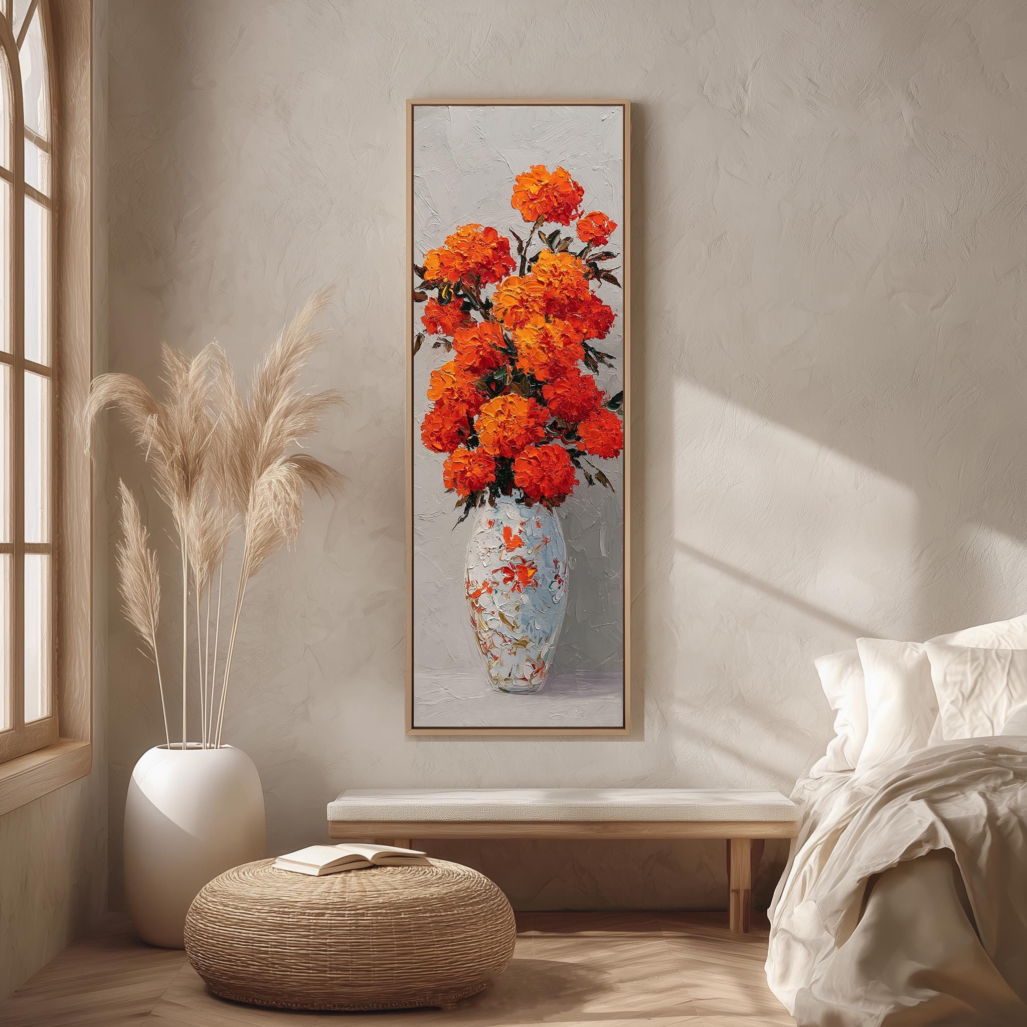 a large painting of a vase filled with orange flowers hanging on a wall in a room with a bed, a wicker ottoman, and a window.