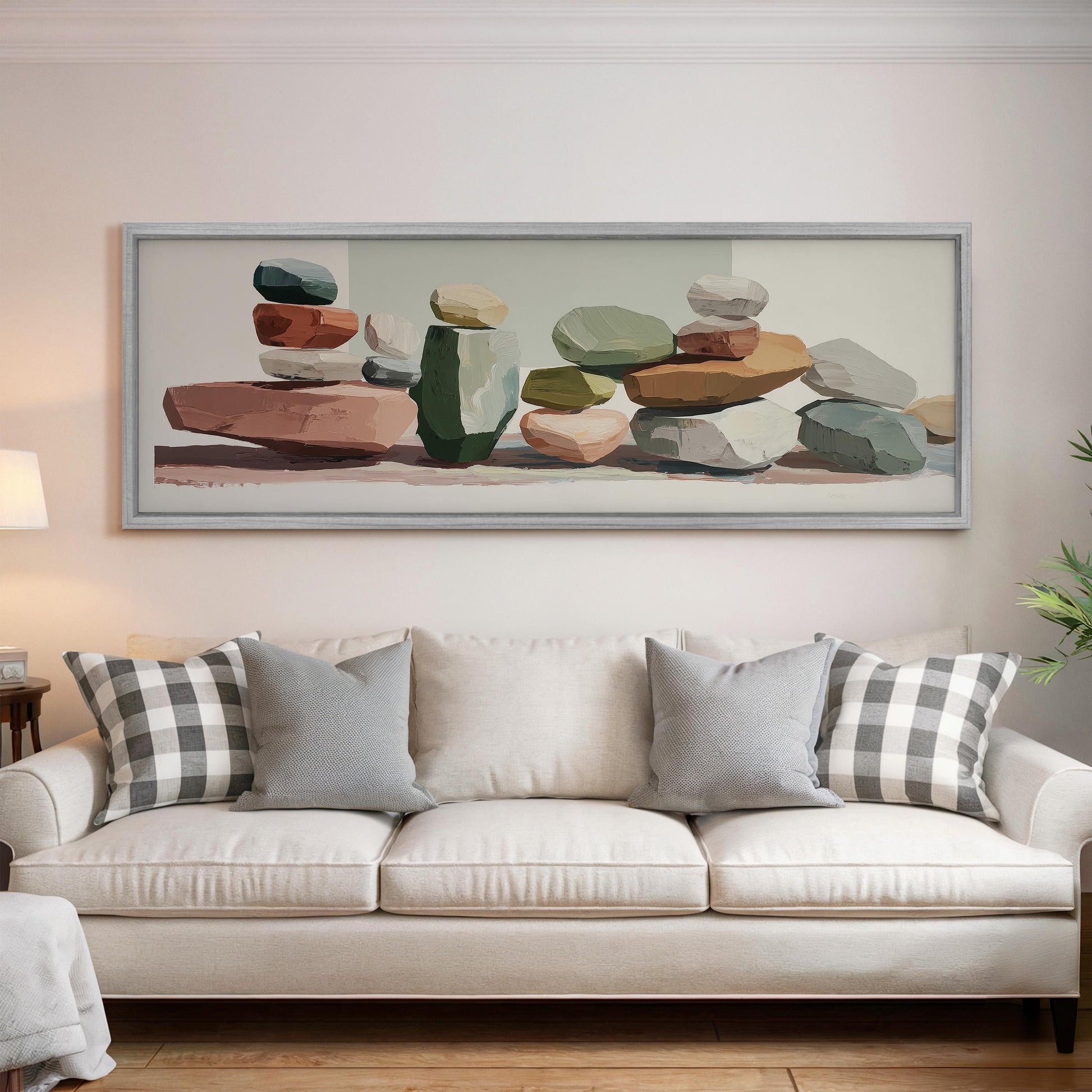 a large framed painting of rocks and stones hanging on a wall above a white couch with patterned throw pillows.