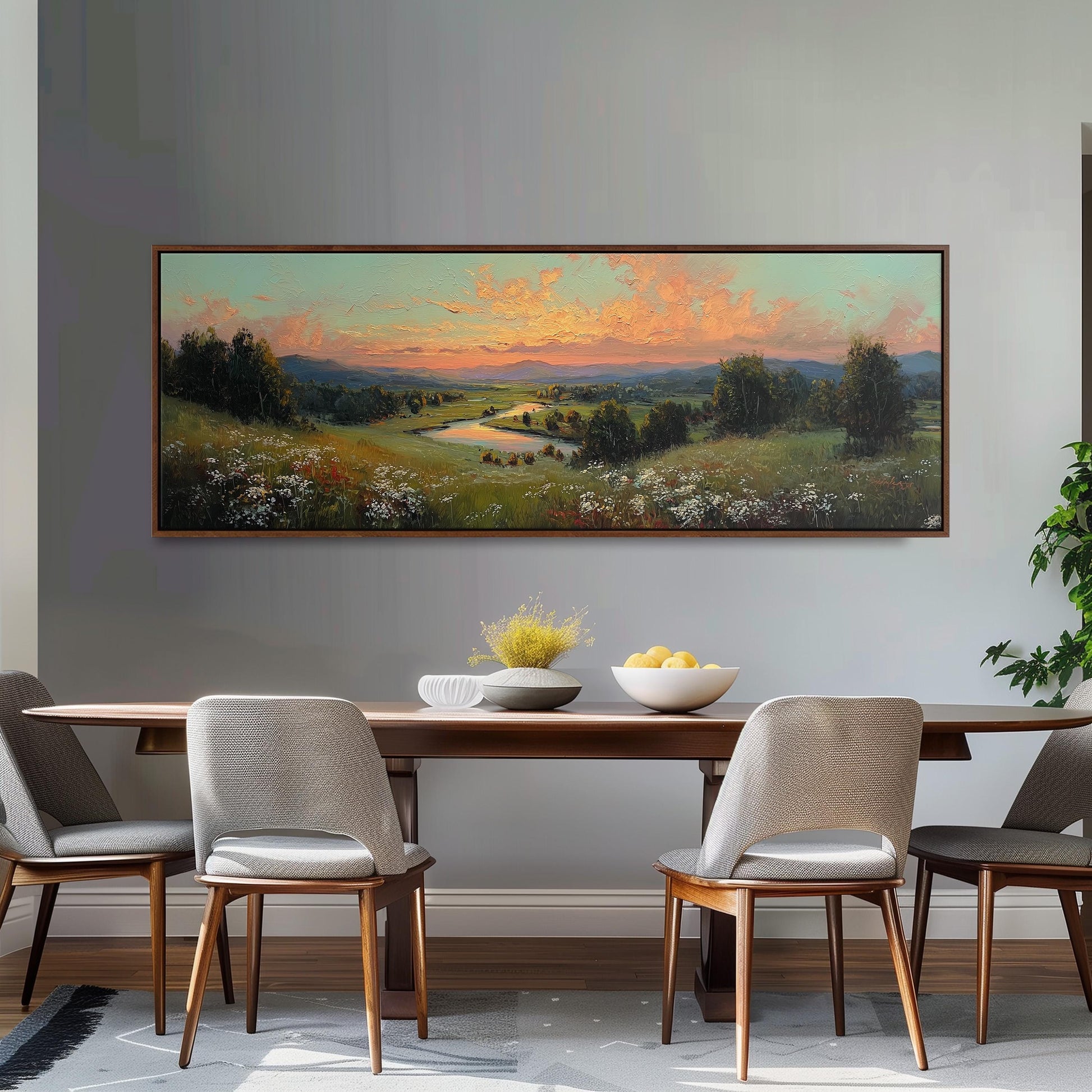 a dining room with a large painting of a countryside landscape hanging on the wall above a wooden dining table with four chairs. The painting depicts a serene countryside scene with rolling hills, a river, and a vibrant sunset sky.