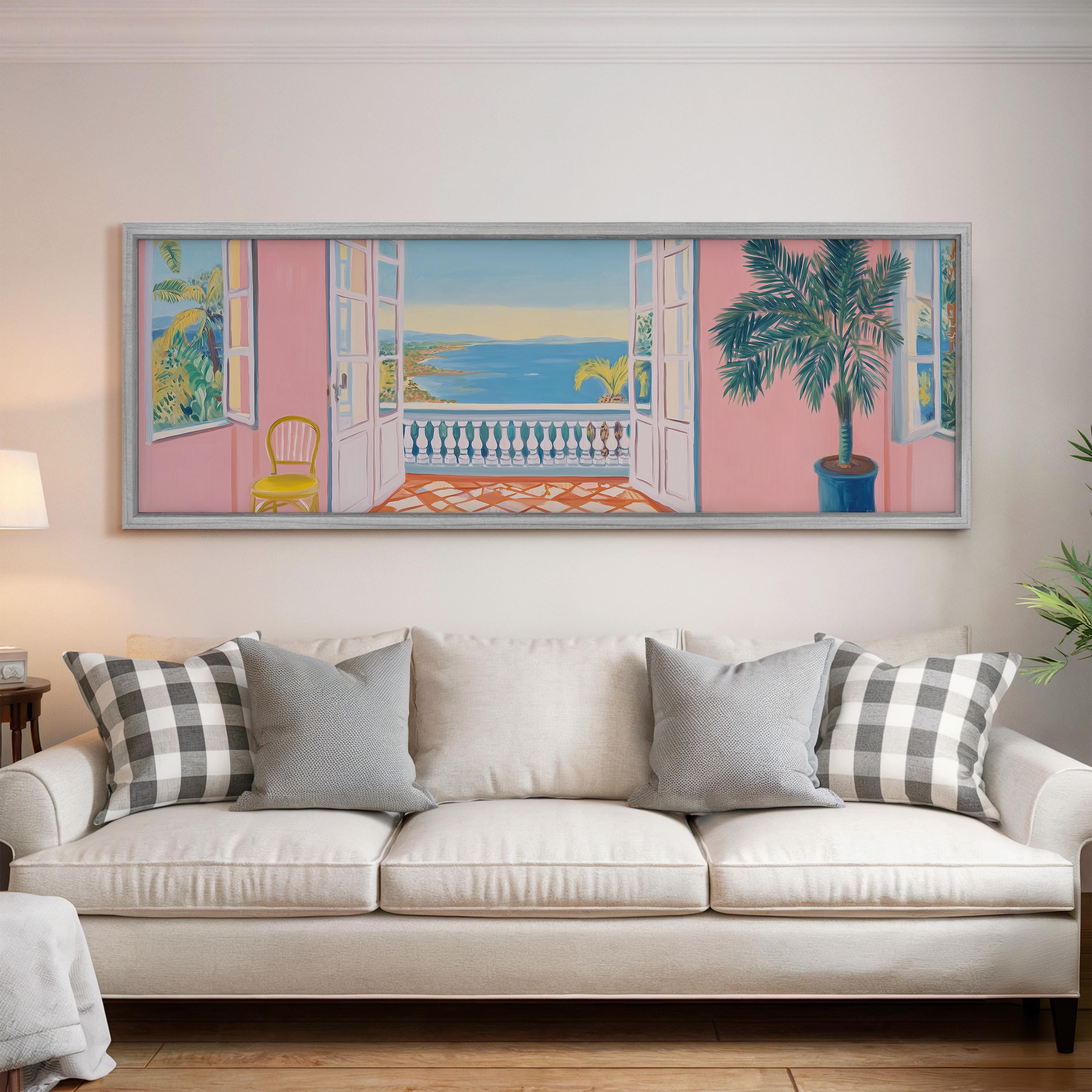 a large, colorful painting of a balcony overlooking the ocean, hanging on a wall above a white sofa with gray and white patterned pillows.