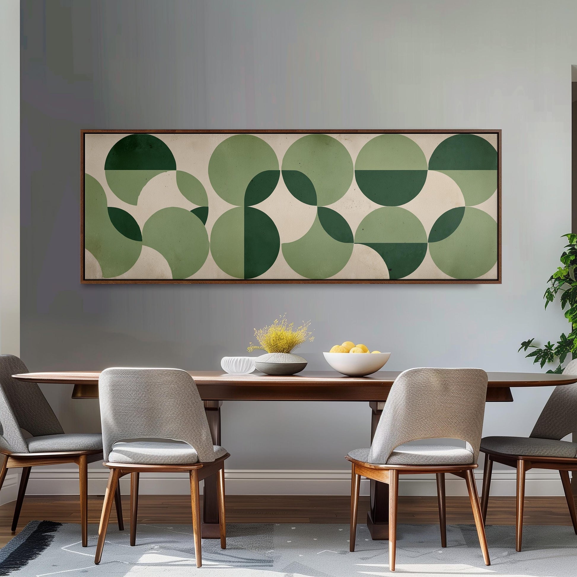a modern dining room with a wooden table and four gray chairs. Above the table, there is a large abstract painting with green and white circles. On the table, there is a bowl of fruit and a vase of flowers.