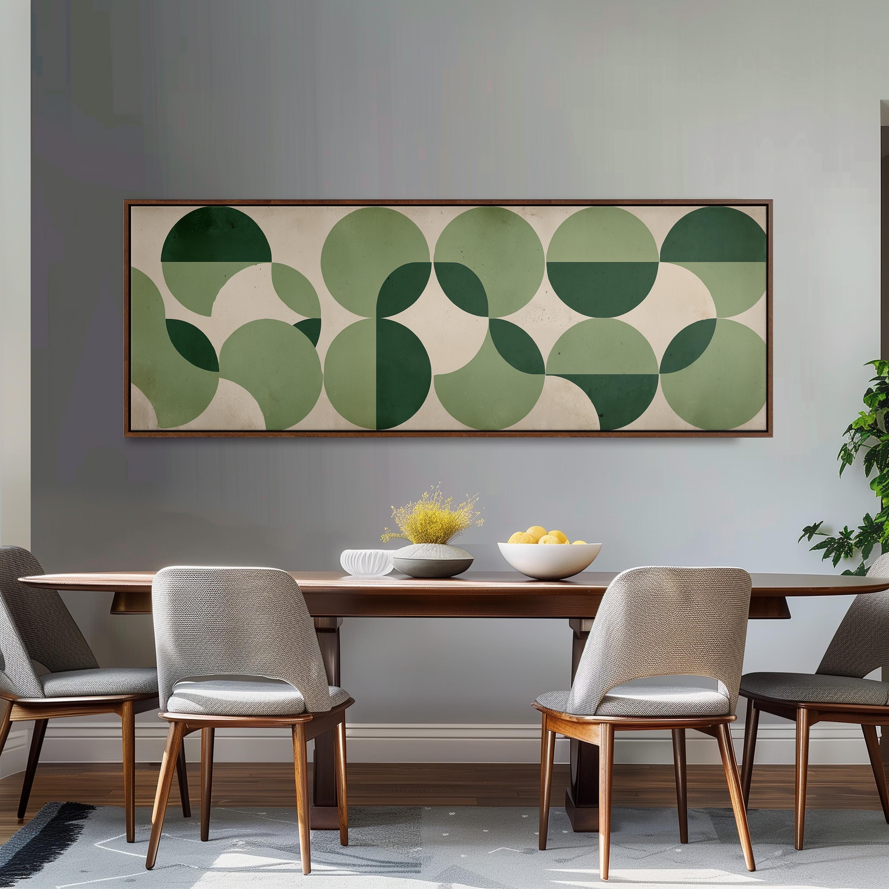 a modern dining room with a wooden table and four gray chairs. Above the table, there is a large abstract painting with green and white circles. On the table, there is a bowl of fruit and a vase of flowers.