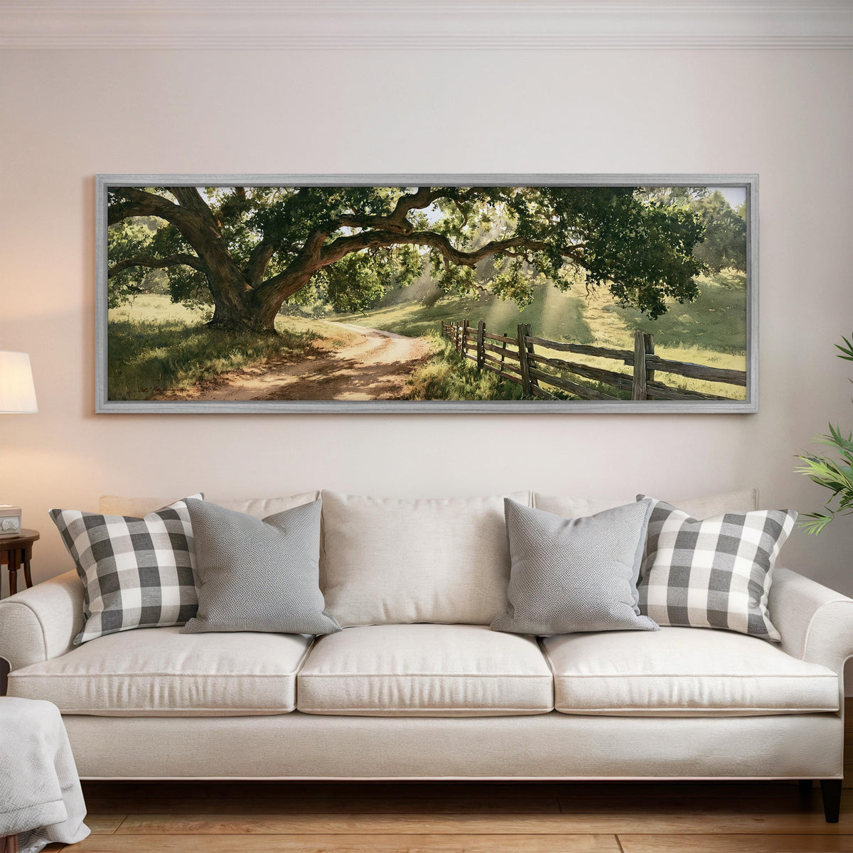 Sunlit country lane with oak trees and a wooden fence panoramic canvas print above a white sofa in a bright living room