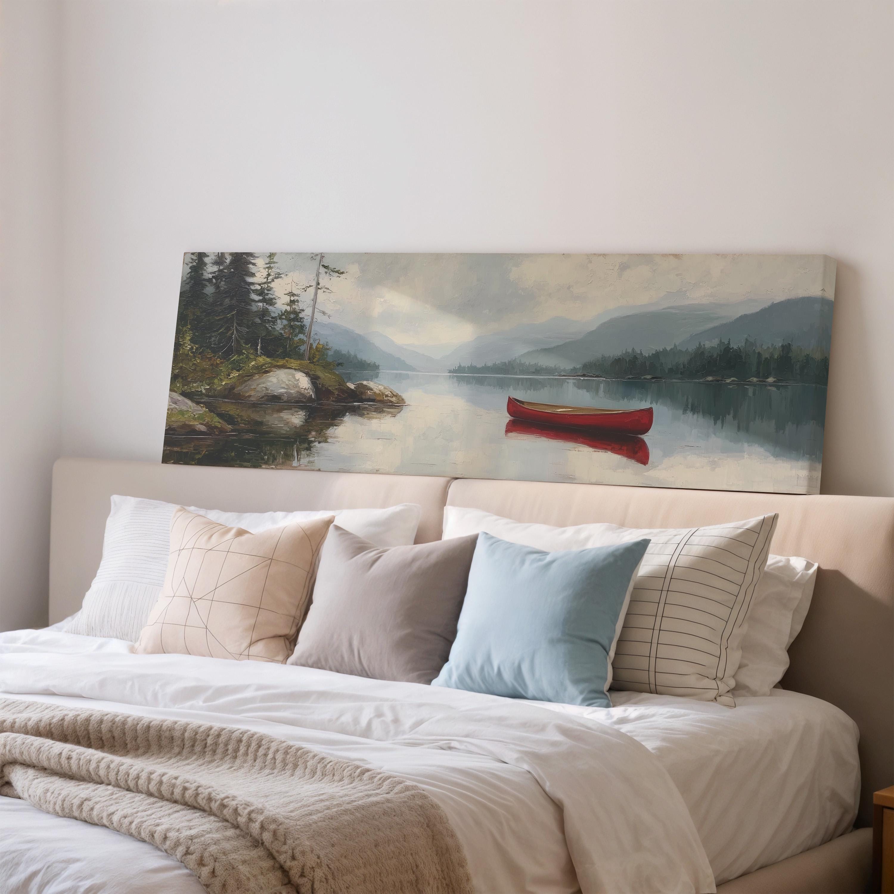 a large painting of a serene landscape with a red canoe on a lake, hanging on a wall above a bed with white bedding and pillows.