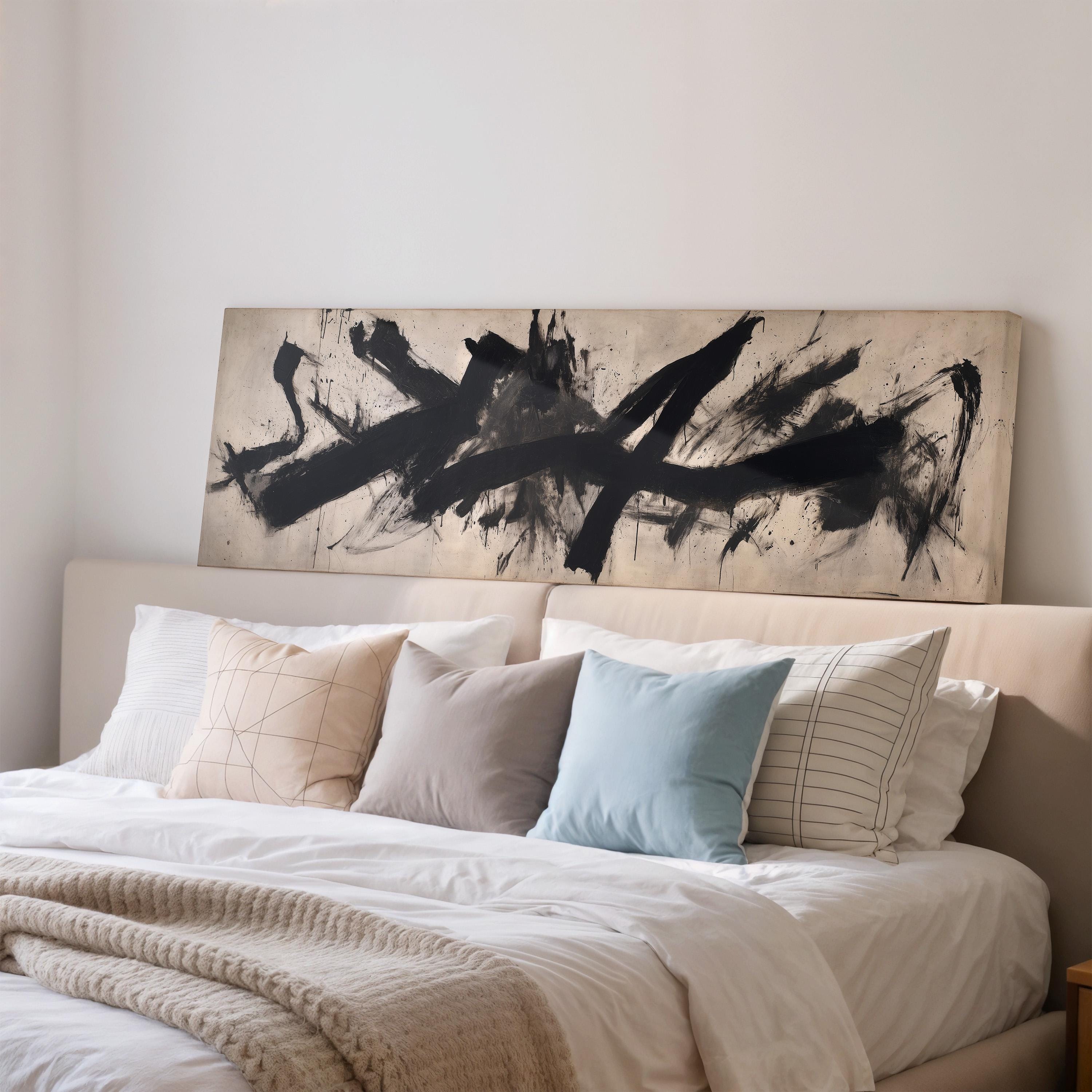 a large bed with a white comforter and a variety of pillows, including a blue pillow and a striped pillow. Above the bed, there is a large abstract painting with bold black lines and splatters.