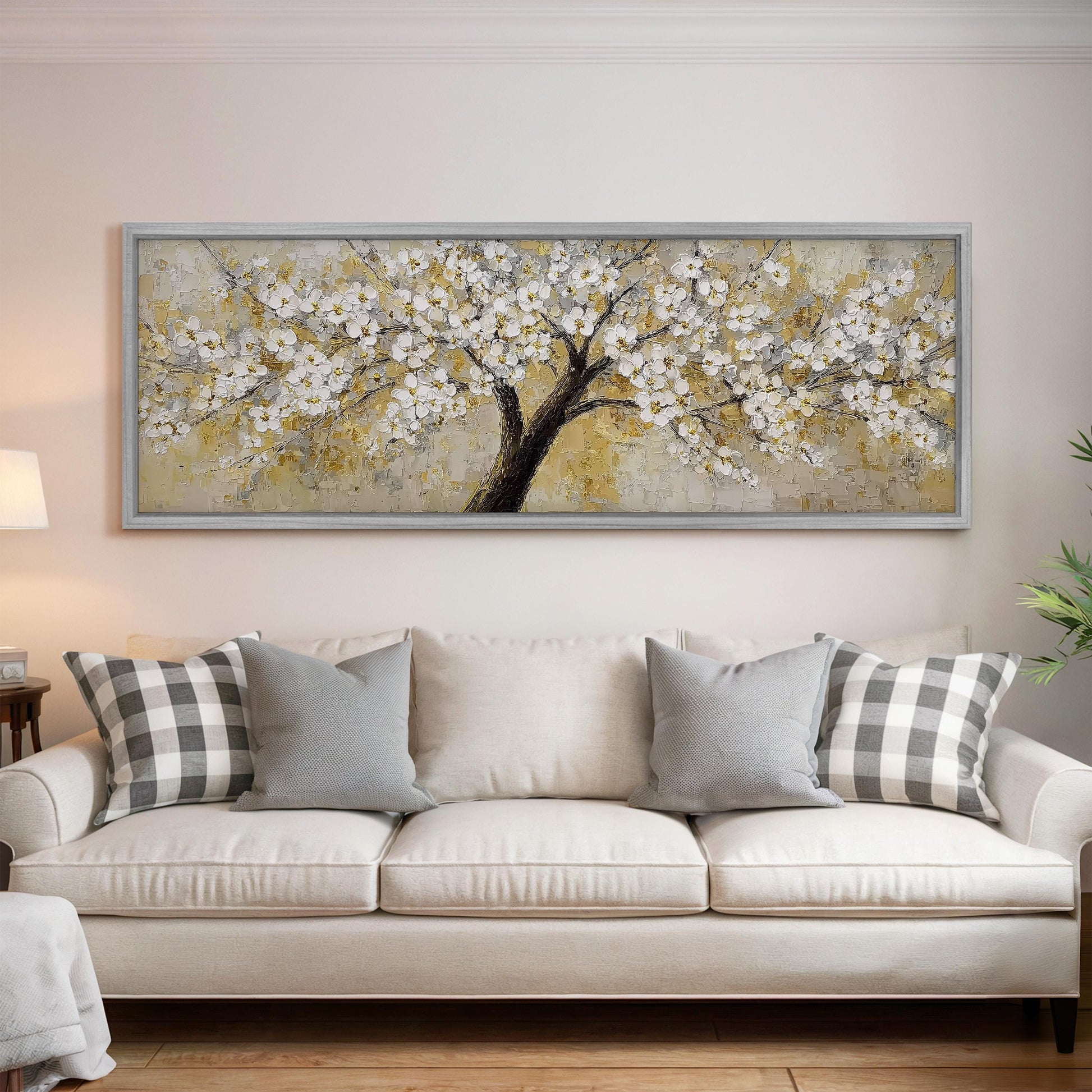 a large, framed painting of a tree with white flowers hanging above a white couch with gray and white pillows.