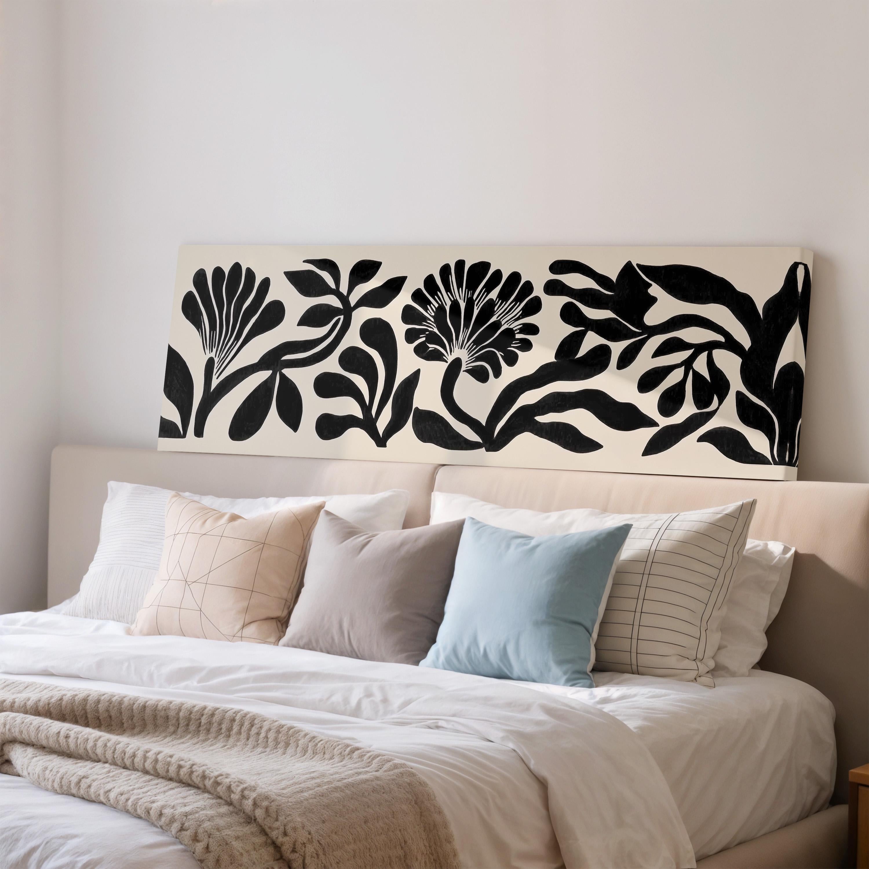 a well-made bed with a white comforter and various pillows, including a blue pillow, a gray pillow, and a striped pillow. Above the bed, there is a large black and white floral print on the wall.