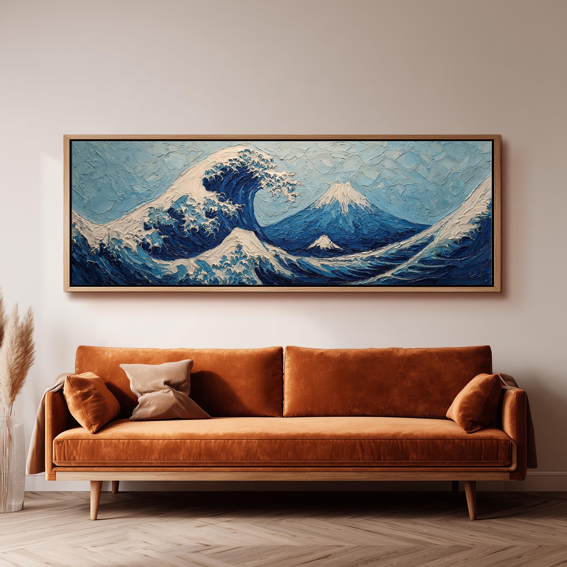 a large, framed painting of a wave with mountains in the background, hanging on a wall above a brown sofa.