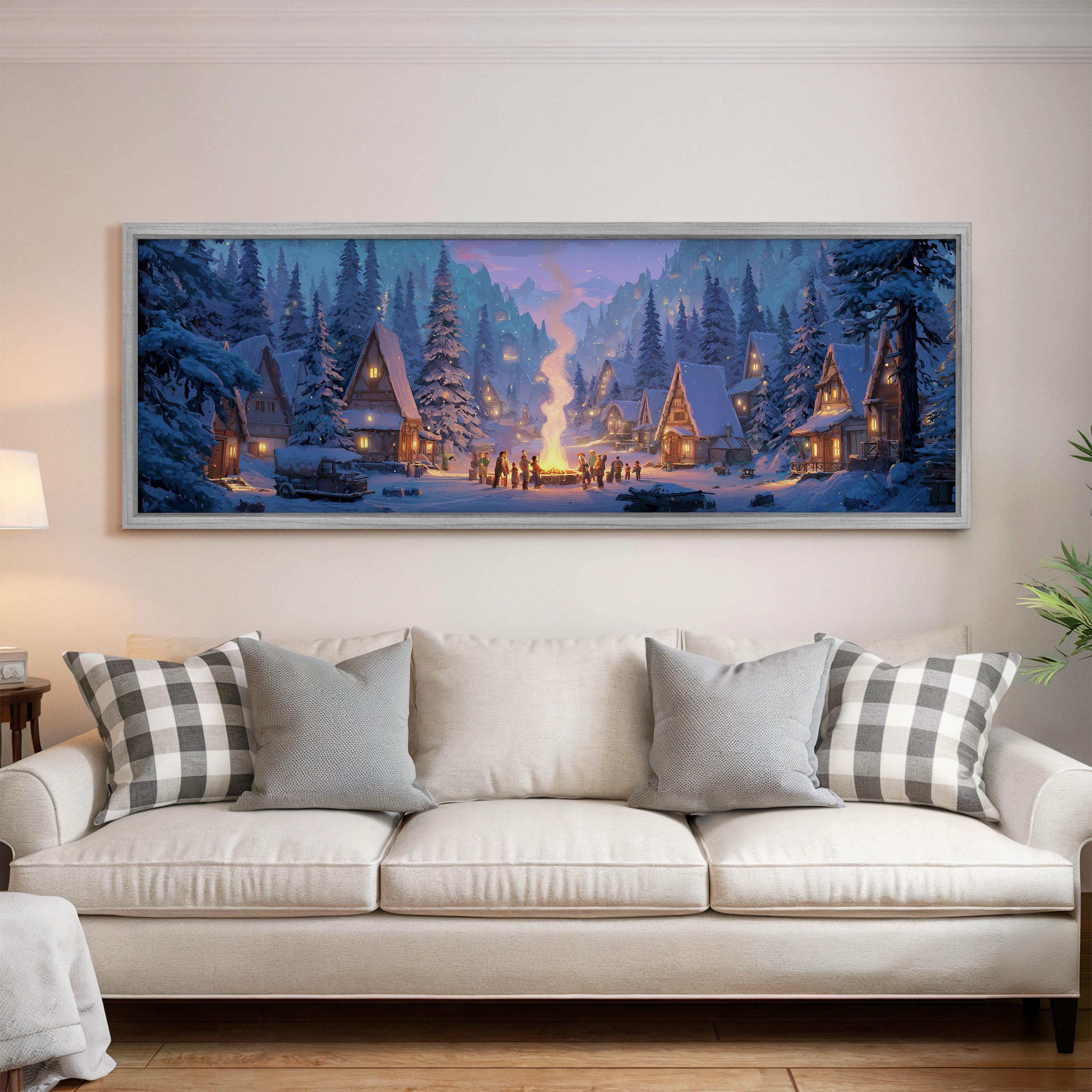 A large, framed painting depicting a snowy village scene with a warm, glowing fire in the center, hanging on a wall above a white couch with patterned throw pillows.