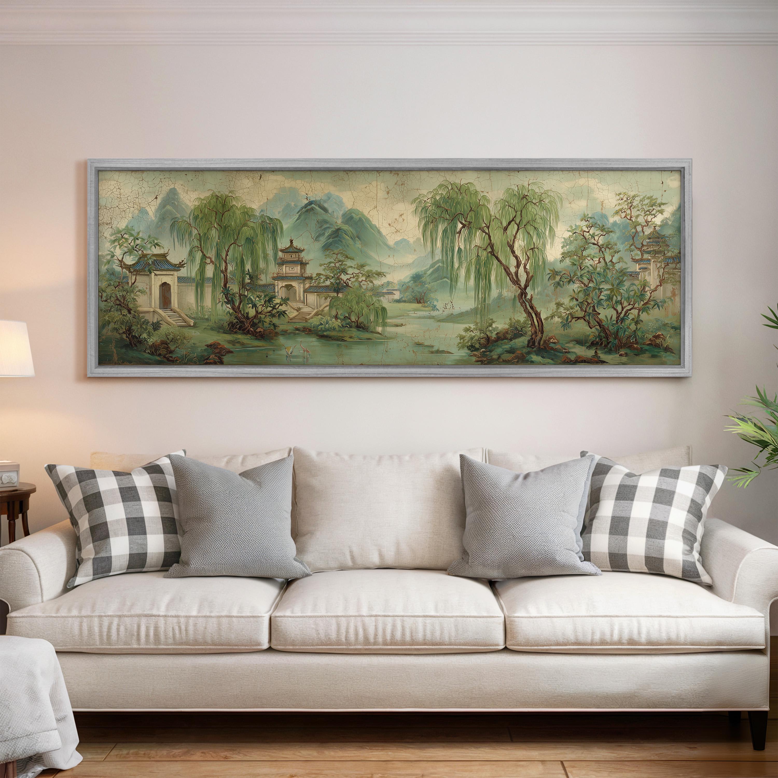 a large, framed painting of a serene landscape hanging on a wall above a white sofa with gray and white patterned pillows.