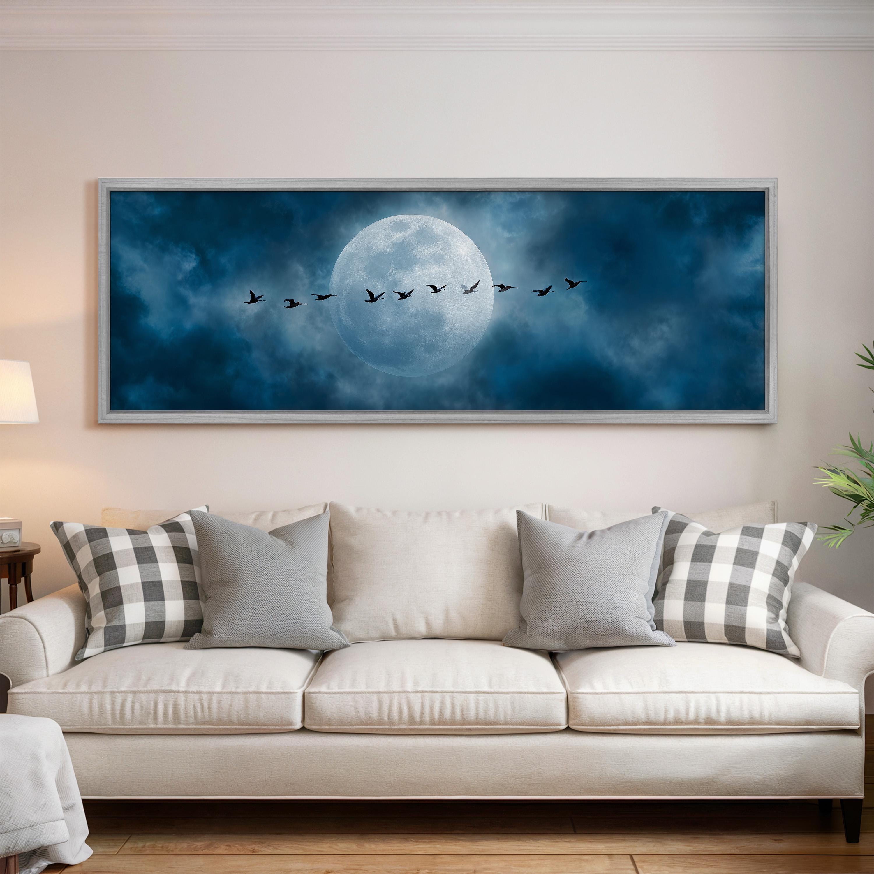 A large framed painting depicting a flock of birds flying across a night sky with a full moon in the background.