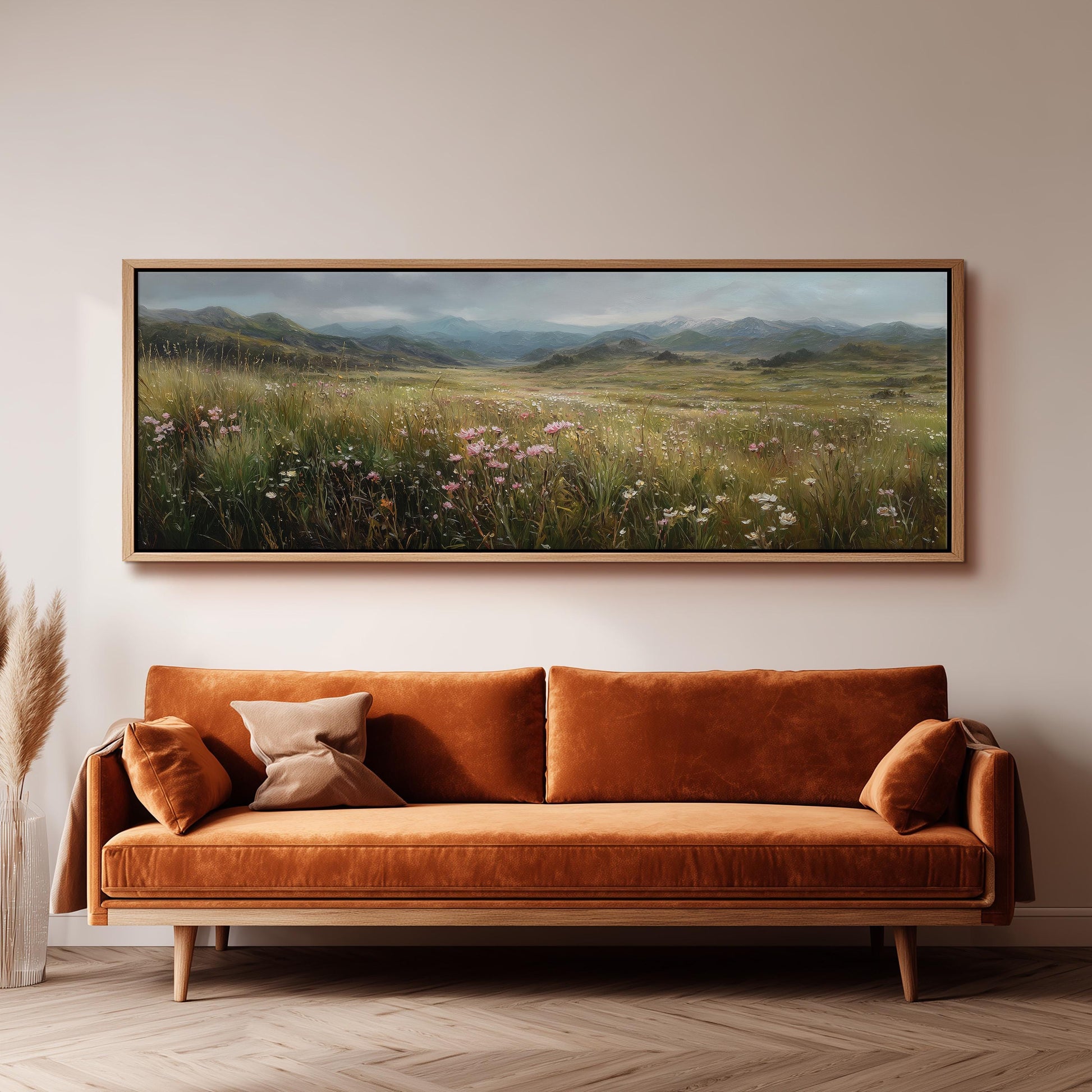 a large, framed painting of a field with flowers hanging on a wall above a brown sofa.