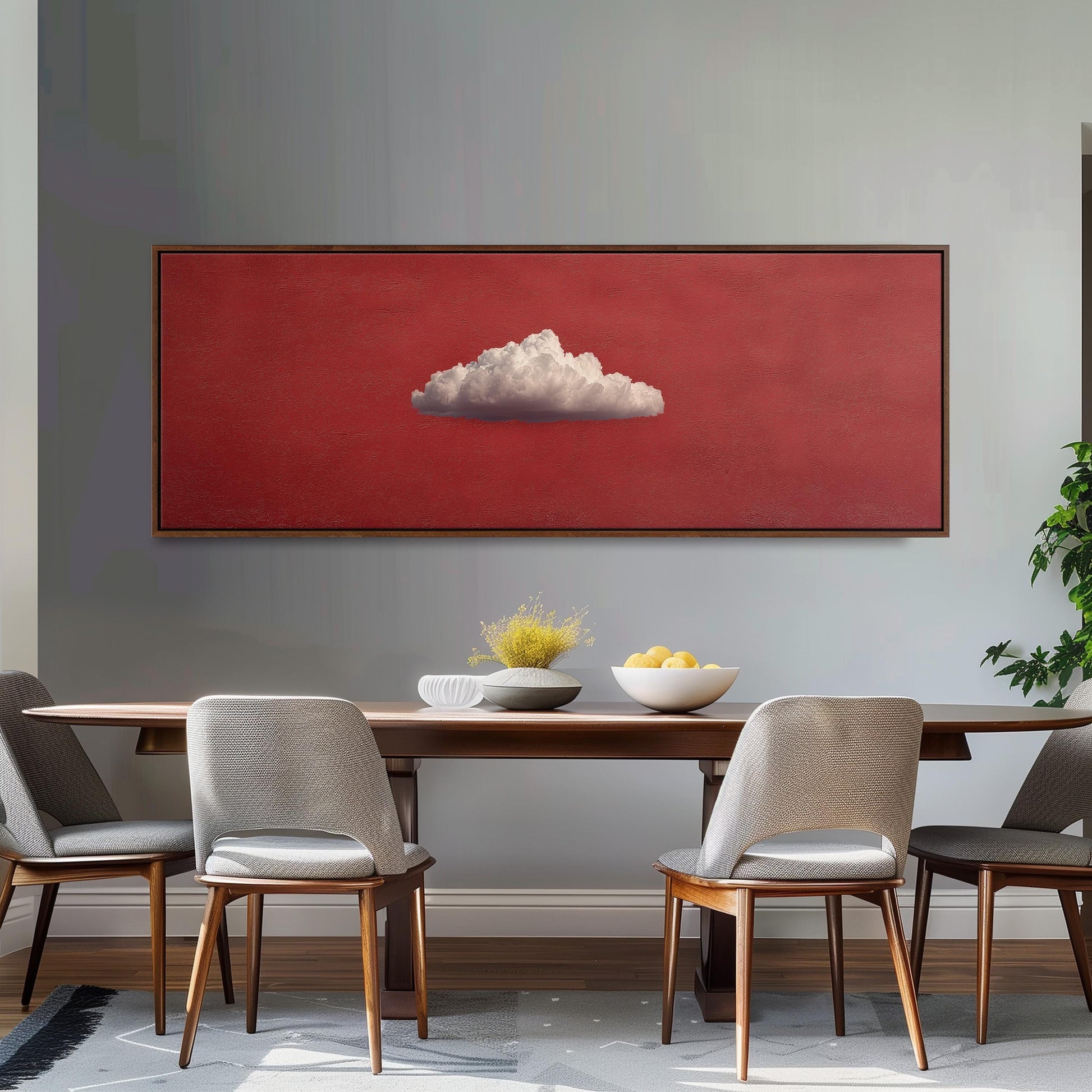 a dining room with a wooden table and four chairs. Above the table, there is a large red painting depicting a cloud on a white background. The table is set with a bowl of fruit and a vase of flowers.