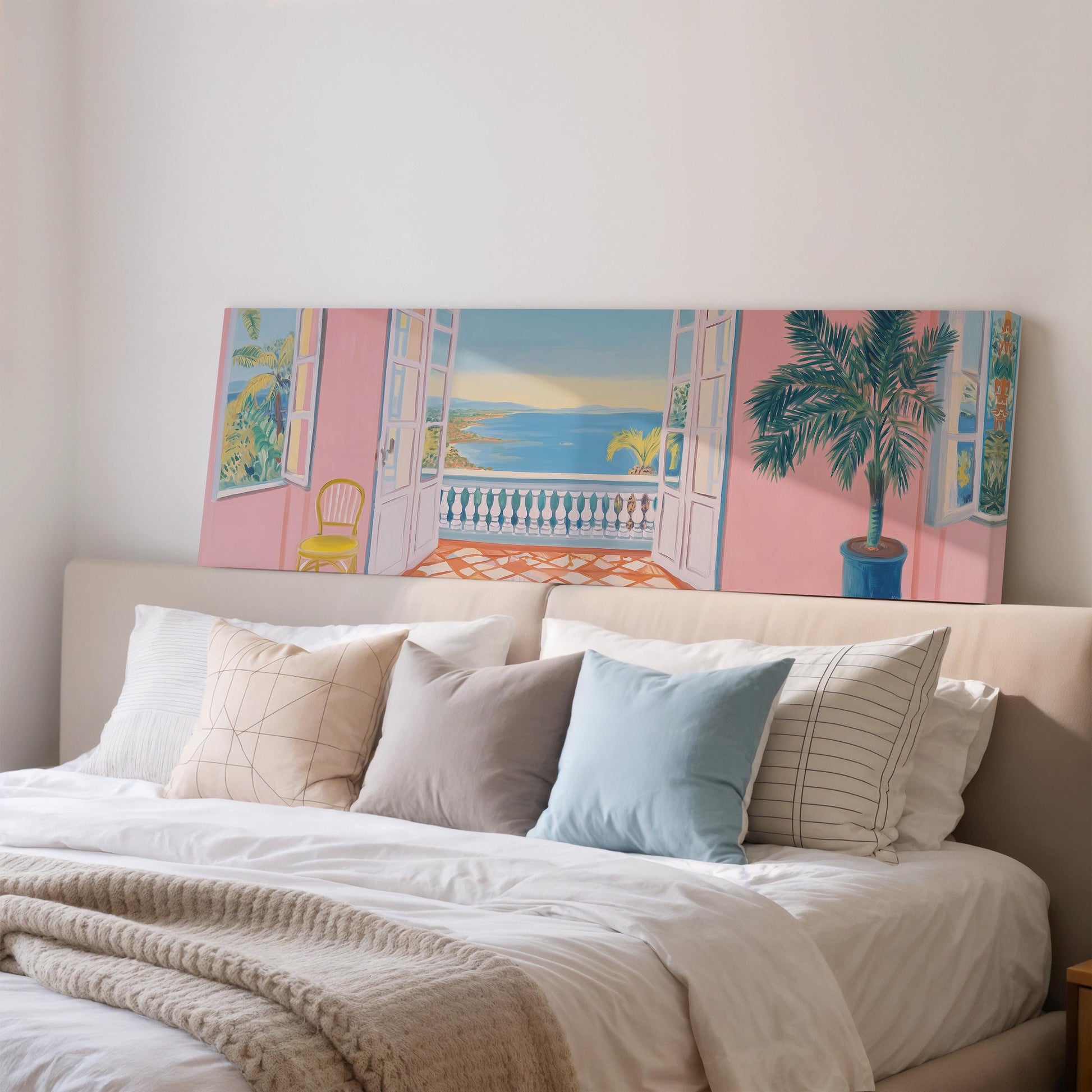 a large bedroom with a bed, a painting of a balcony overlooking the ocean, and a window with a plant on the sill.