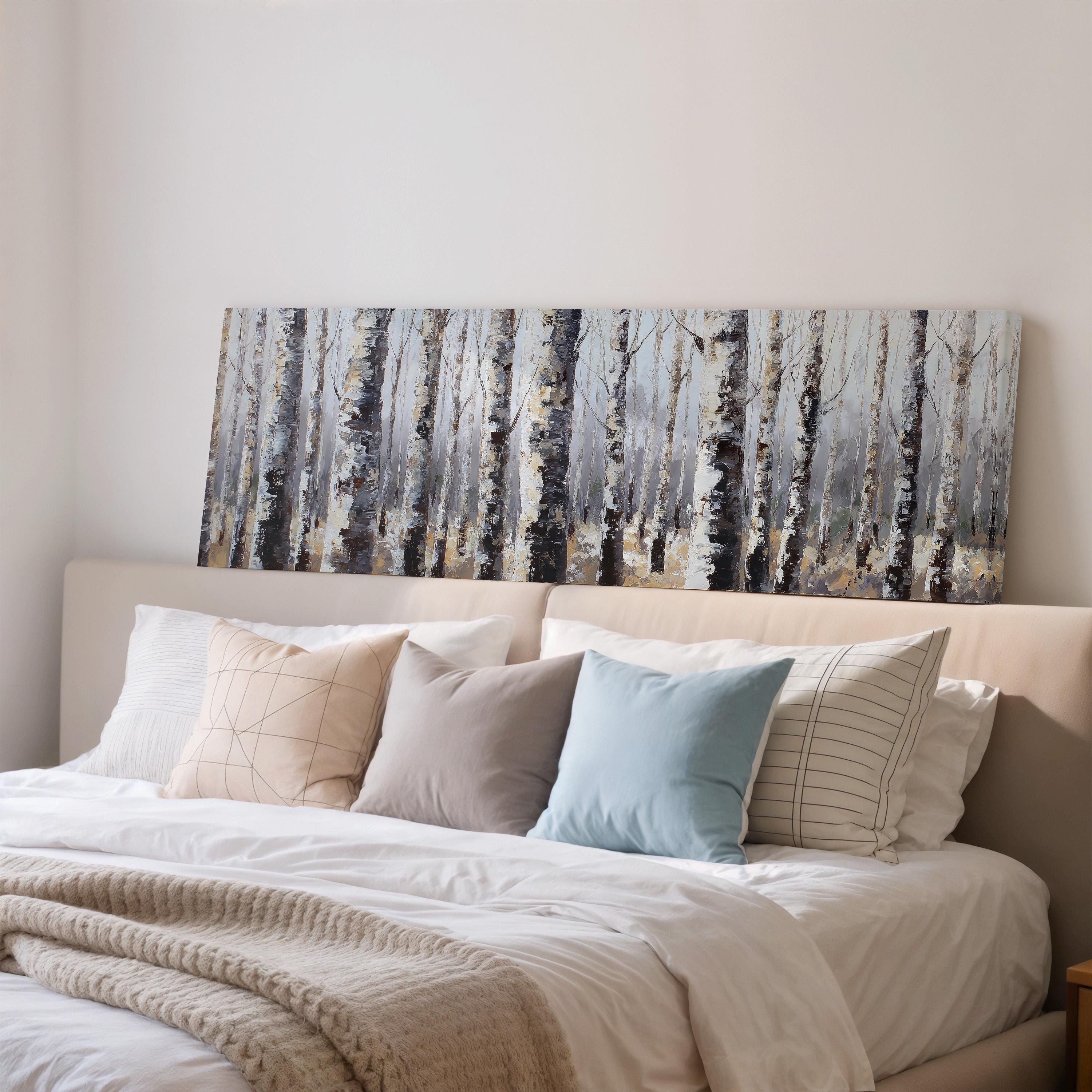 a cozy bedroom with a large bed adorned with white linens and a variety of colorful throw pillows. Above the bed, there is a painting of a forest scene, adding a touch of nature to the room's decor.