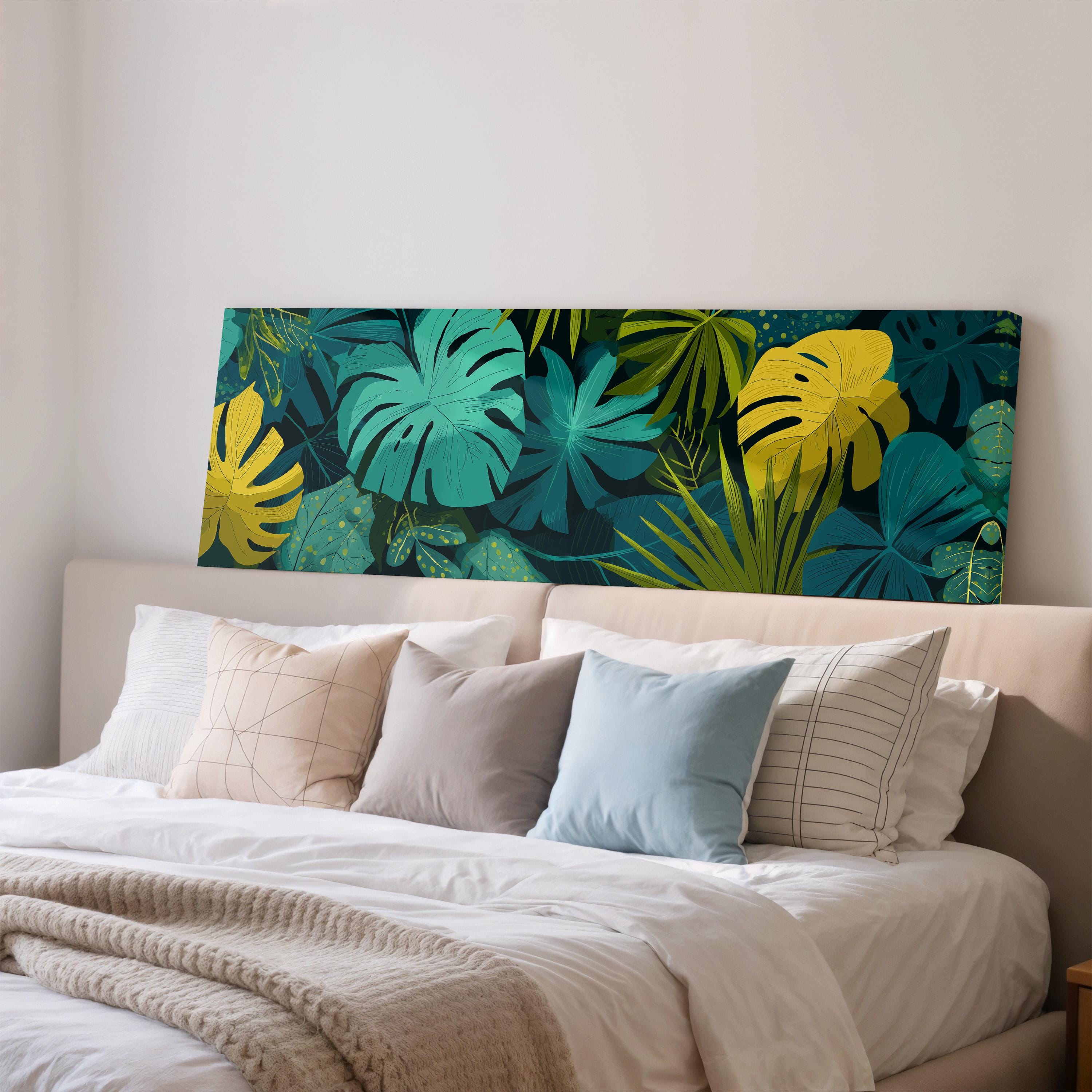 a large bed with a white comforter and a variety of colorful pillows. The bed is positioned against a wall with a large canvas print featuring a tropical plant design in shades of green and yellow.