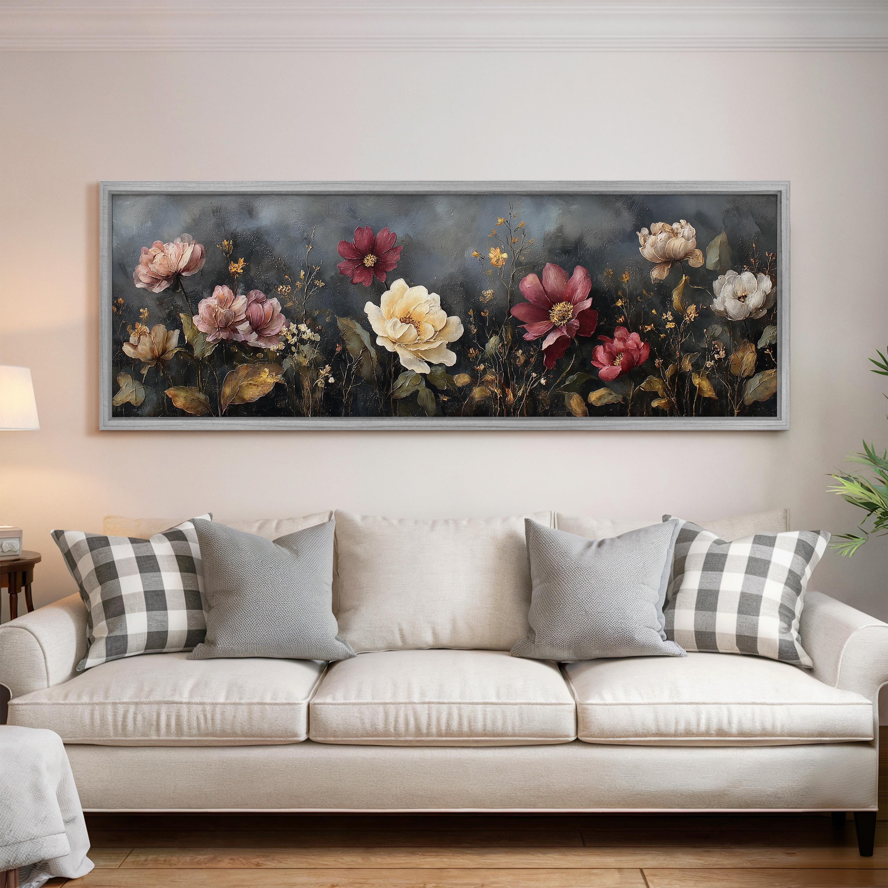a large, framed painting of flowers hanging on a wall above a white couch with gray and white plaid throw pillows.