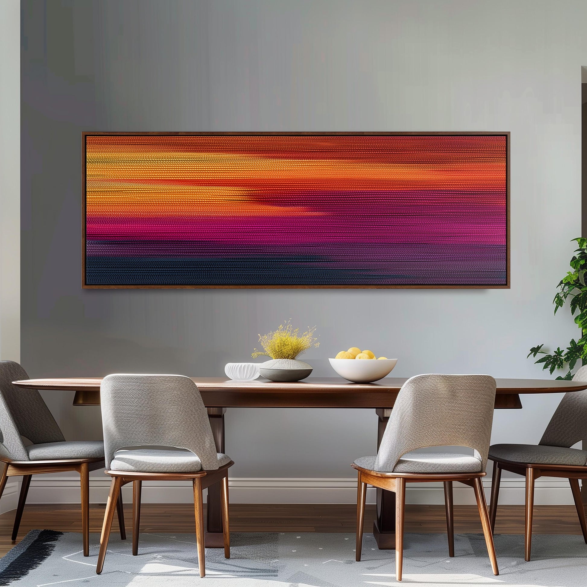 a dining room with a wooden table and four chairs. Above the table, there is a large, colorful abstract painting hanging on the wall. The table is set with a bowl of fruit and a vase of flowers, creating a warm and inviting atmosphere.