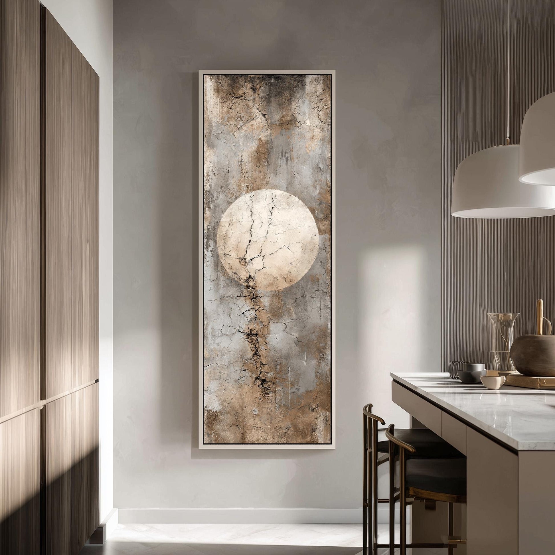 a modern kitchen with a large abstract painting hanging on the wall above a counter. The painting has a textured, earthy color palette and depicts a large, cracked circle. The kitchen is well-lit, with a pendant light hanging above the counter and a vase on the counter.