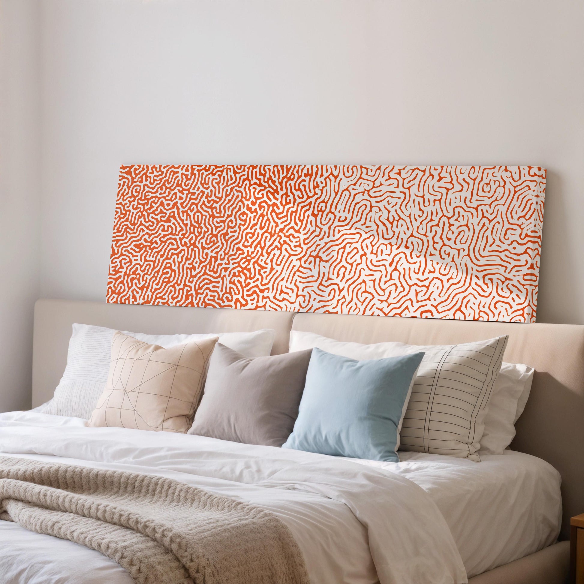 a well-made bed with a white comforter and a variety of pillows in different colors and patterns. Above the bed, there is a large abstract painting with a pattern of orange and white swirls.