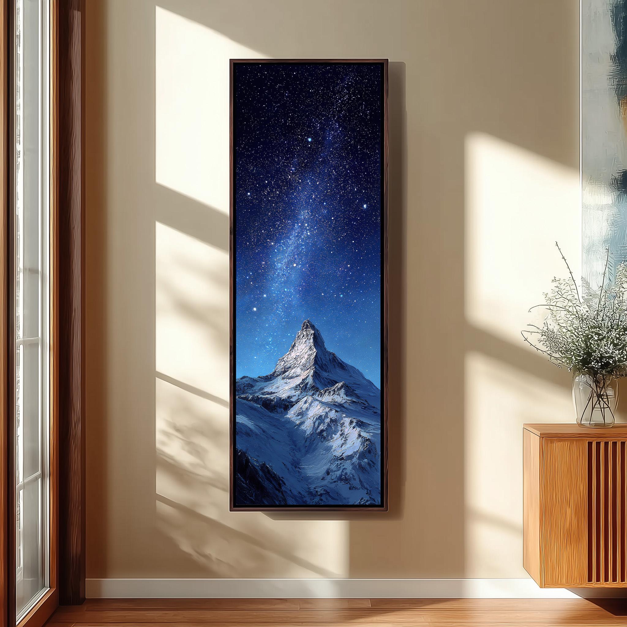 a large framed painting of a snow-capped mountain peak under a starry night sky, hanging on a wall in a room with a wooden cabinet and a vase of flowers.