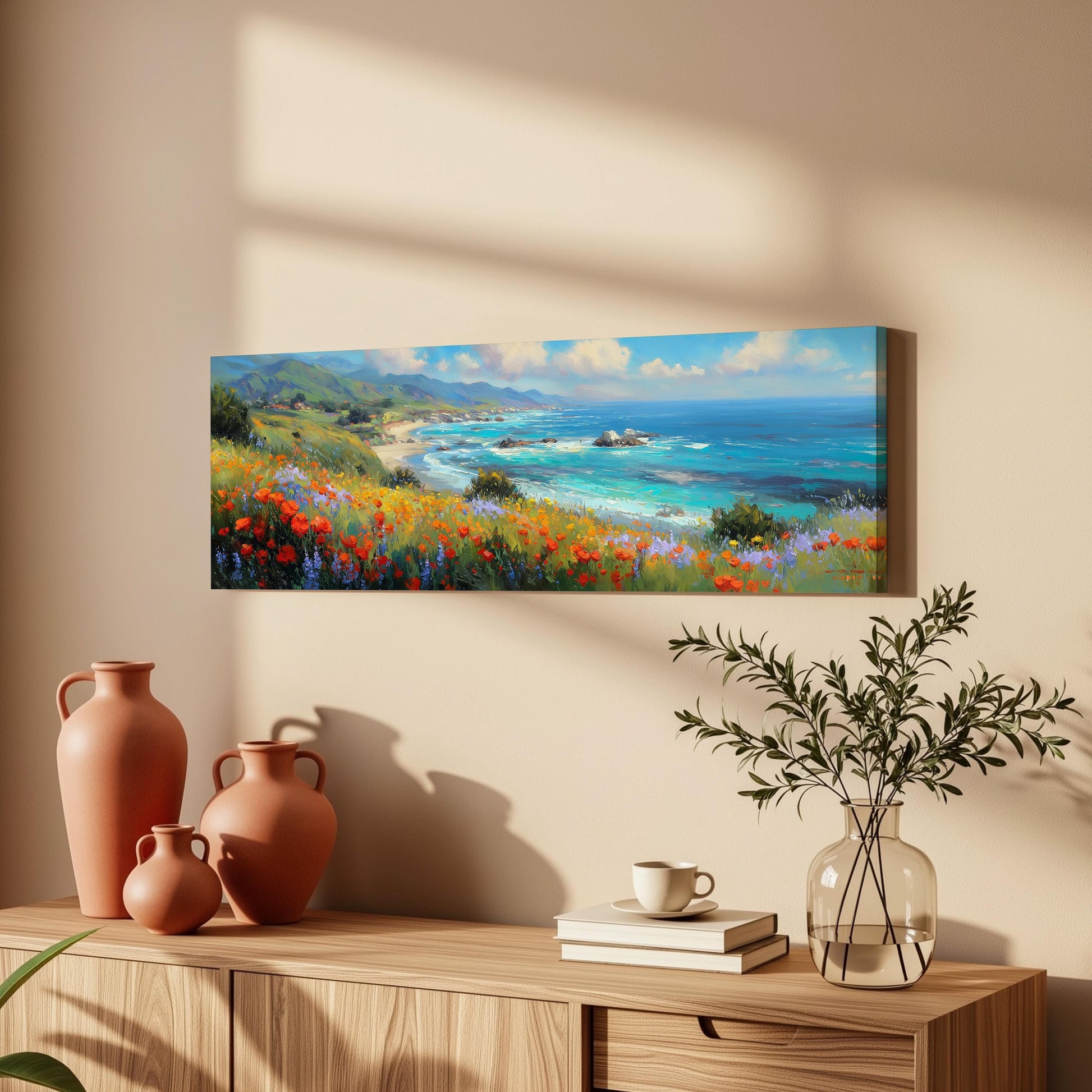 a serene coastal landscape with a vibrant field of flowers, a calm ocean, and a picturesque beach. The painting is hung on a wall above a wooden dresser, which has a vase of flowers, a stack of books, and a coffee cup on it.