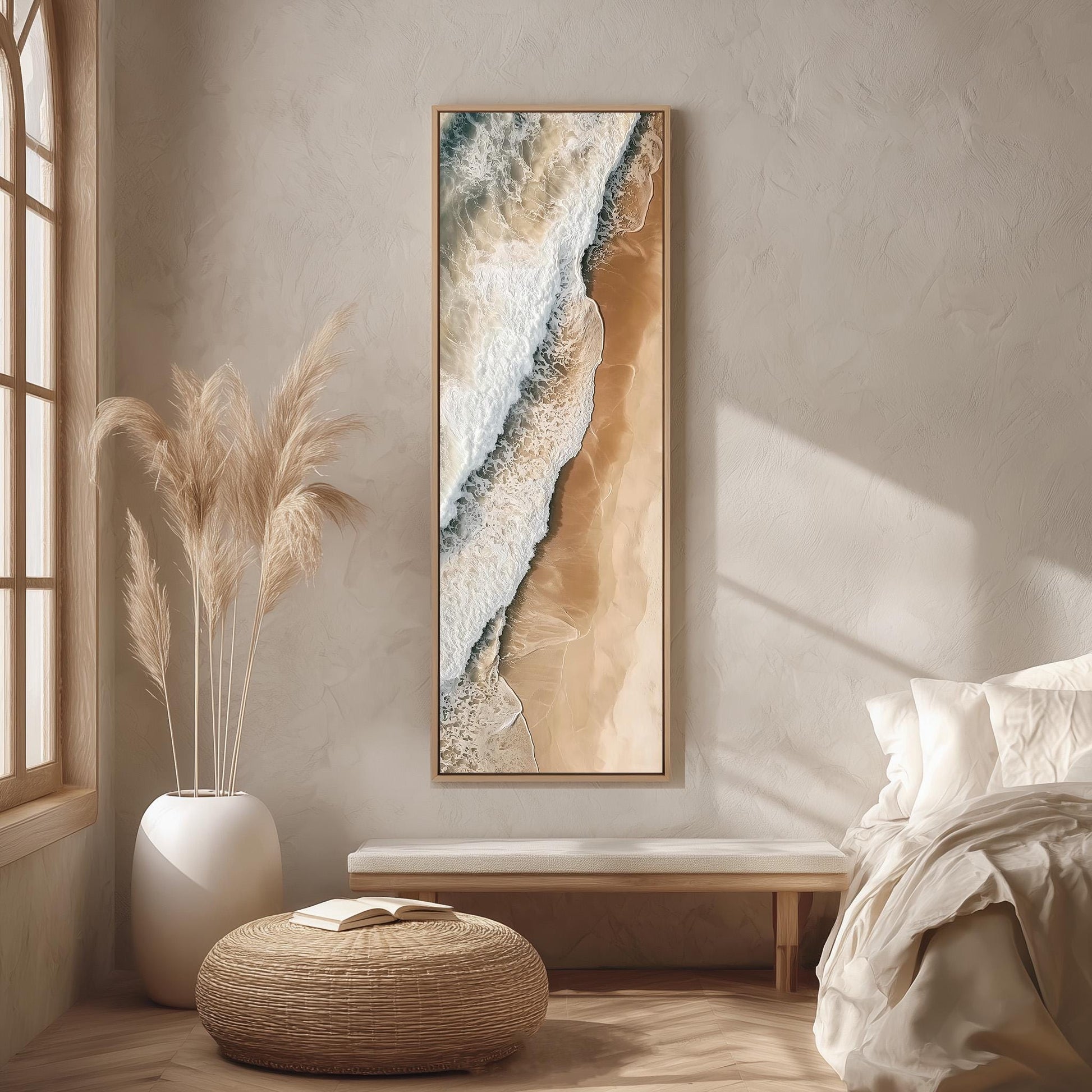 a serene and minimalist bedroom interior with a large window, a white bed, a woven ottoman, and a framed artwork of a beach scene on the wall.