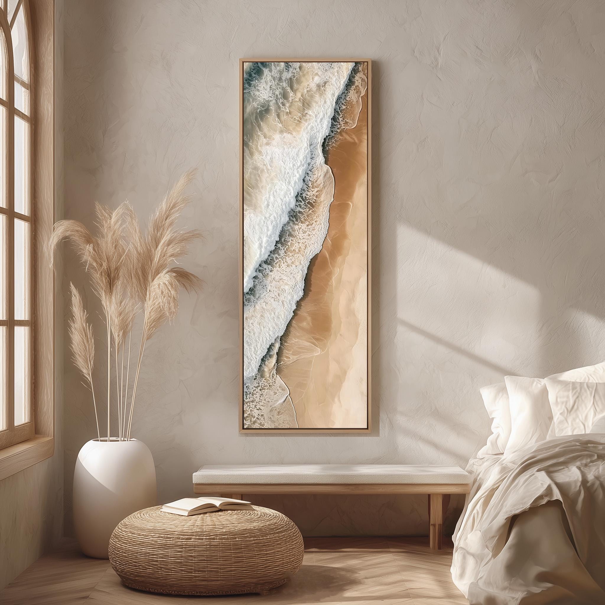 a serene and minimalist bedroom interior with a large window, a white bed, a woven ottoman, and a framed artwork of a beach scene on the wall.