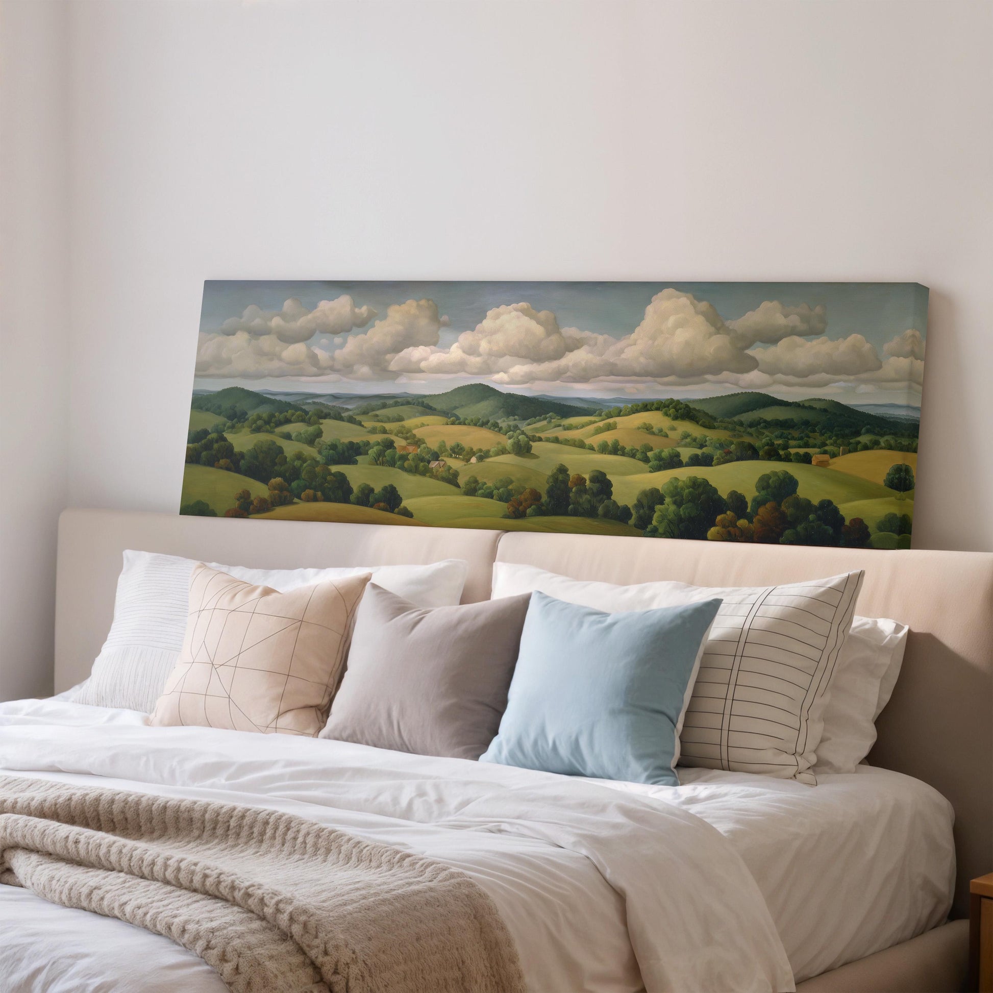 a large landscape painting hanging on a wall above a bed with white pillows and a gray blanket.