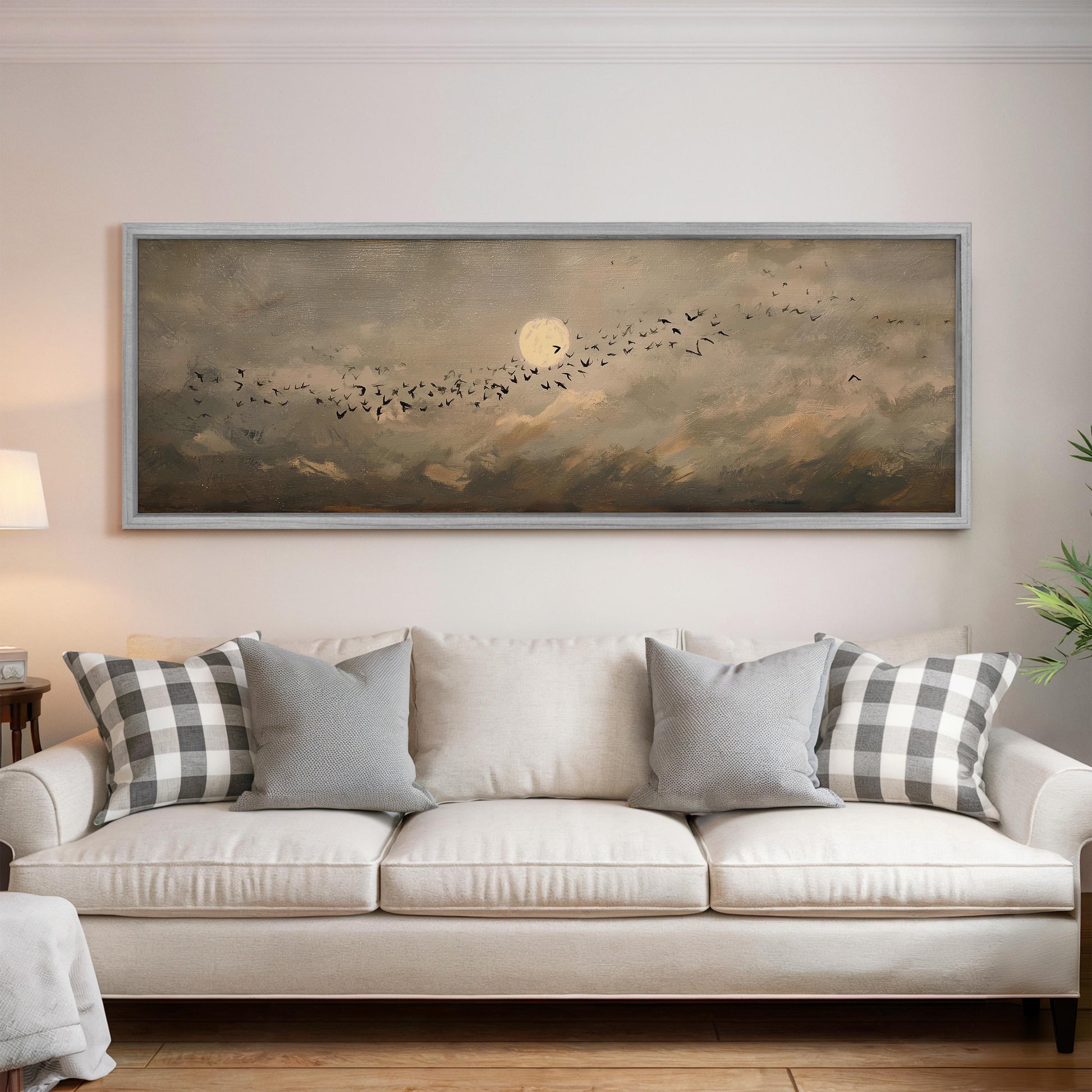 a large painting of a flock of birds flying over a cloudy sky, hanging on a wall above a white sofa with gray and white patterned pillows.
