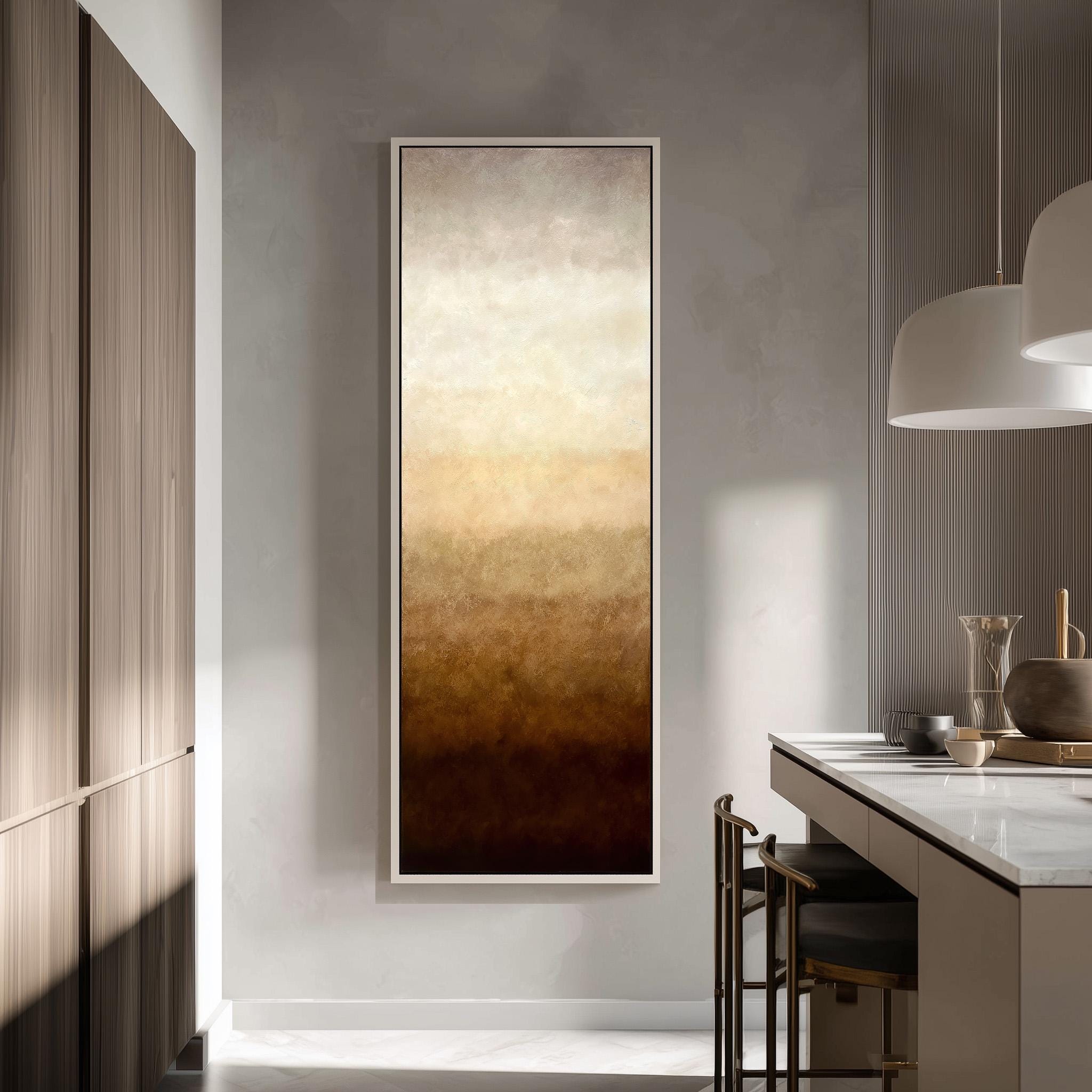 a modern kitchen with a large, abstract painting hanging on the wall above a counter. The painting has a warm, earthy color palette with shades of brown and orange. The kitchen is well-lit, with natural light streaming in from a window on the left side of the image. The counter is equipped with a sink and a few decorative items, such as a vase and a bowl.