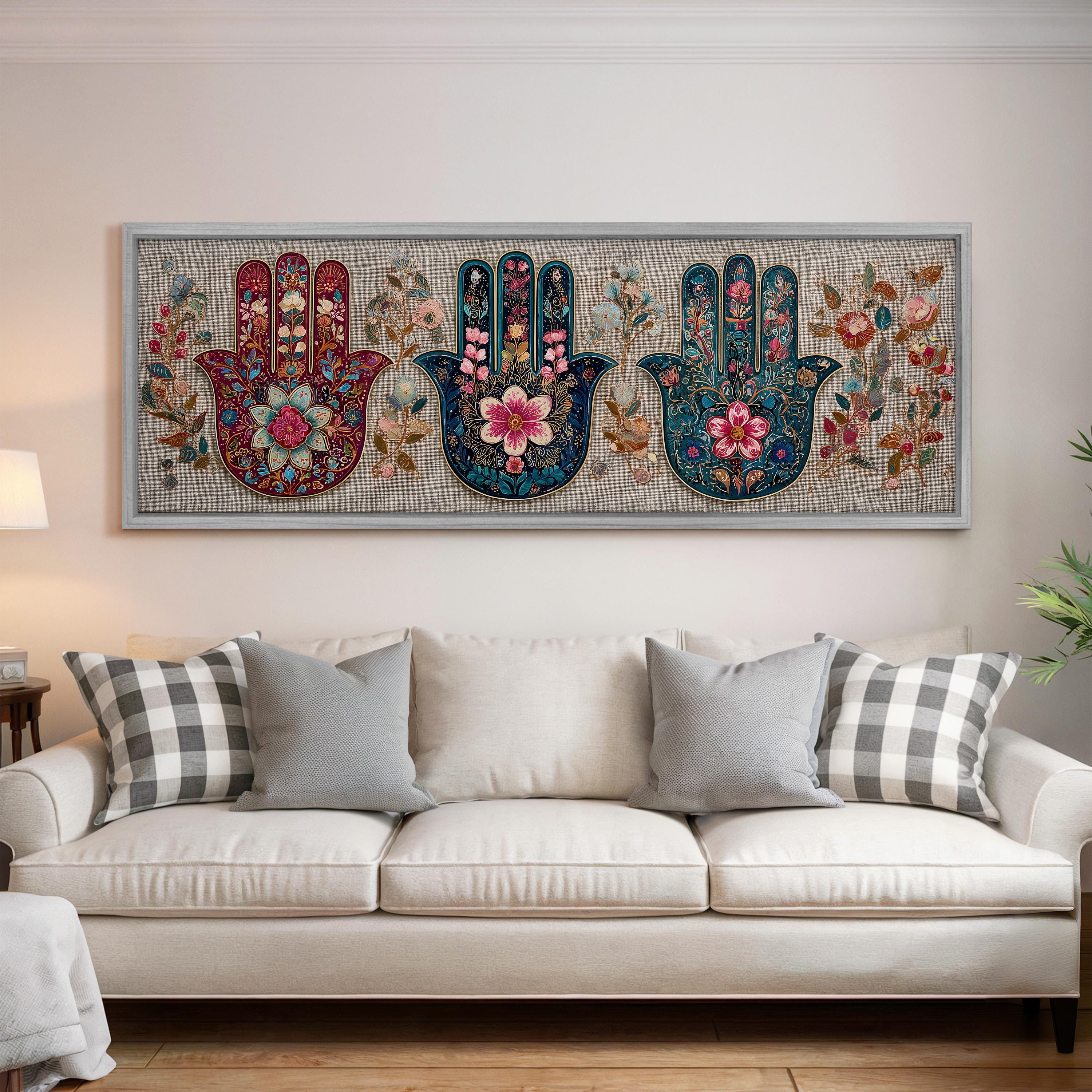 a large, colorful, and intricate painting of three hands with floral designs on a wall above a white couch in a living room setting.