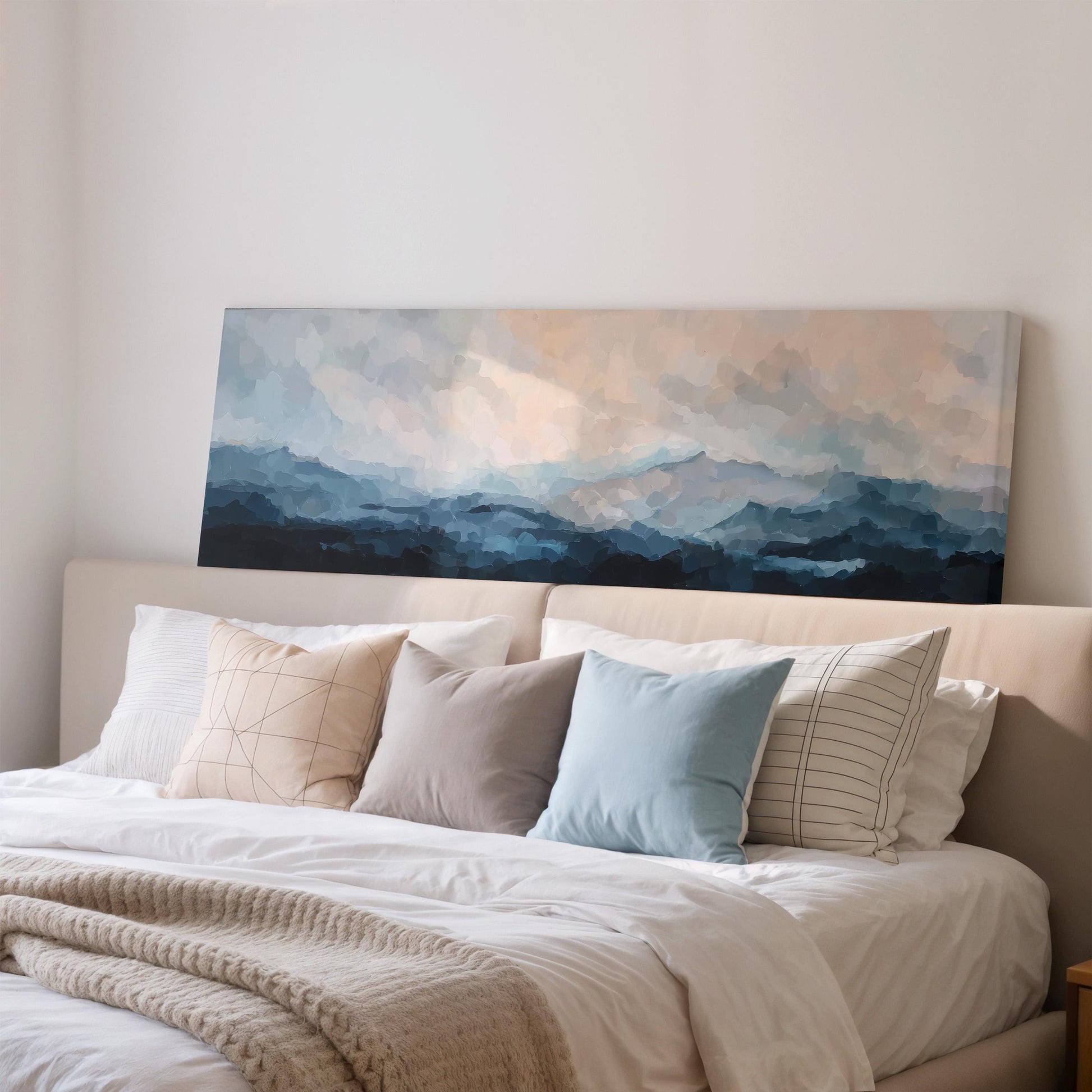 a large painting of a mountain landscape hanging on a wall above a bed with white bedding and various pillows.