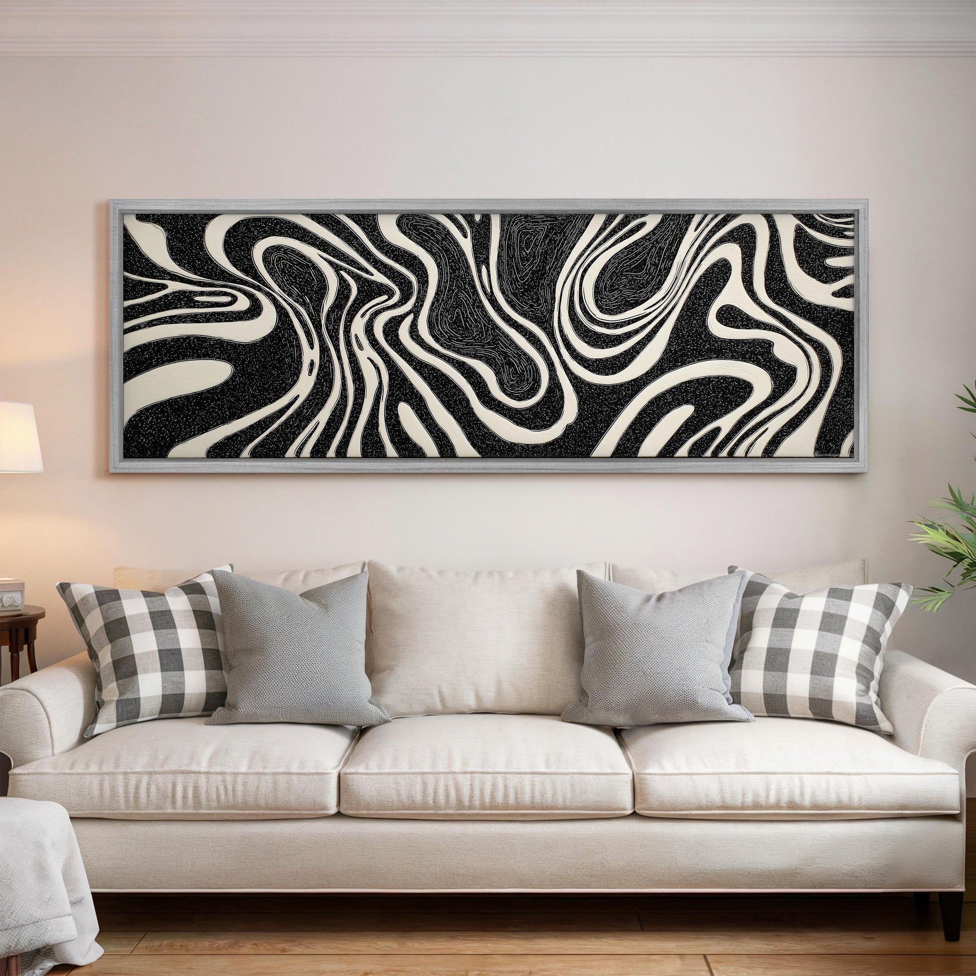 a large, white couch with gray and white plaid throw pillows, and a framed abstract artwork with black and white swirls hanging above it on a white wall.