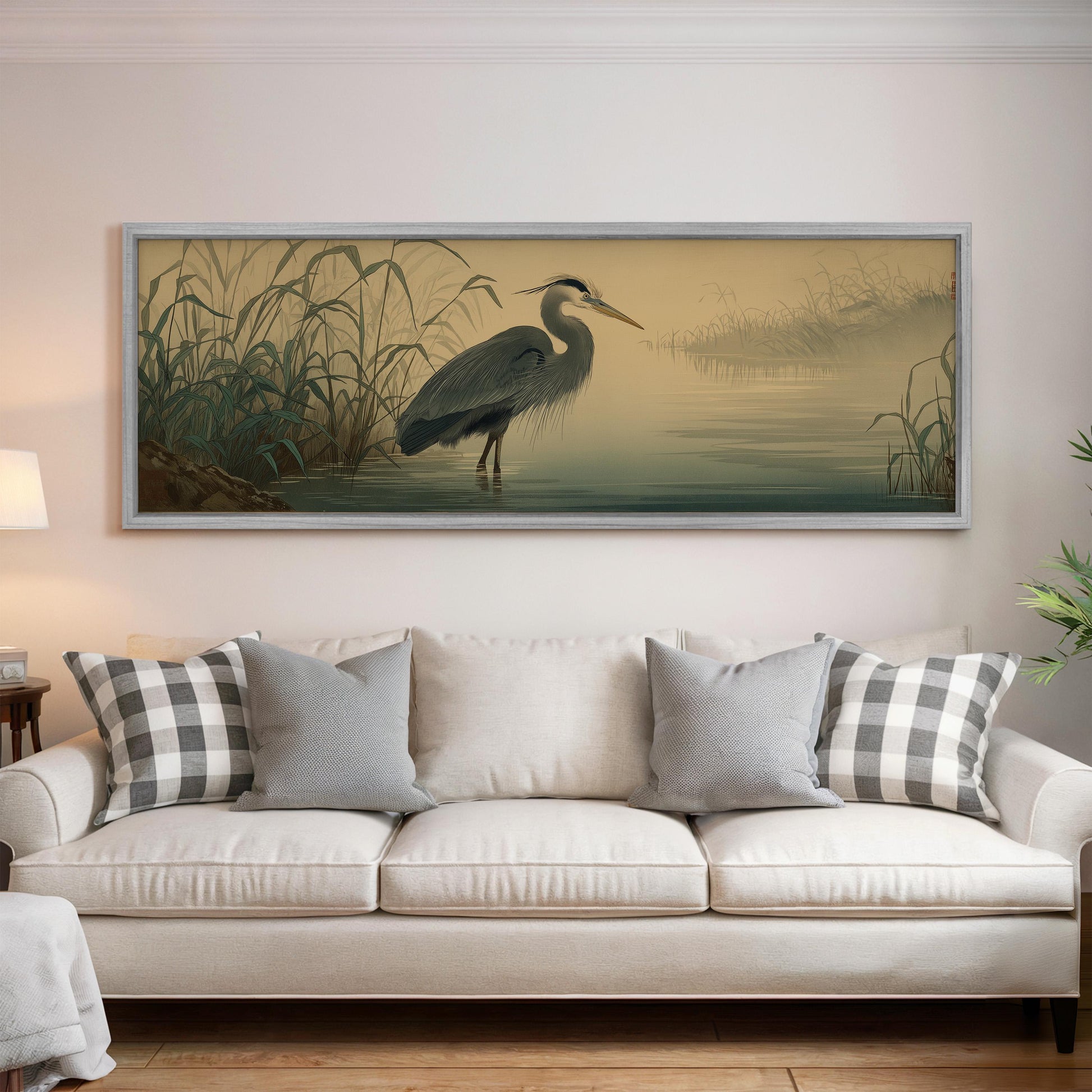 a large framed painting of a heron standing in a body of water, hanging on a wall above a white sofa with decorative pillows.