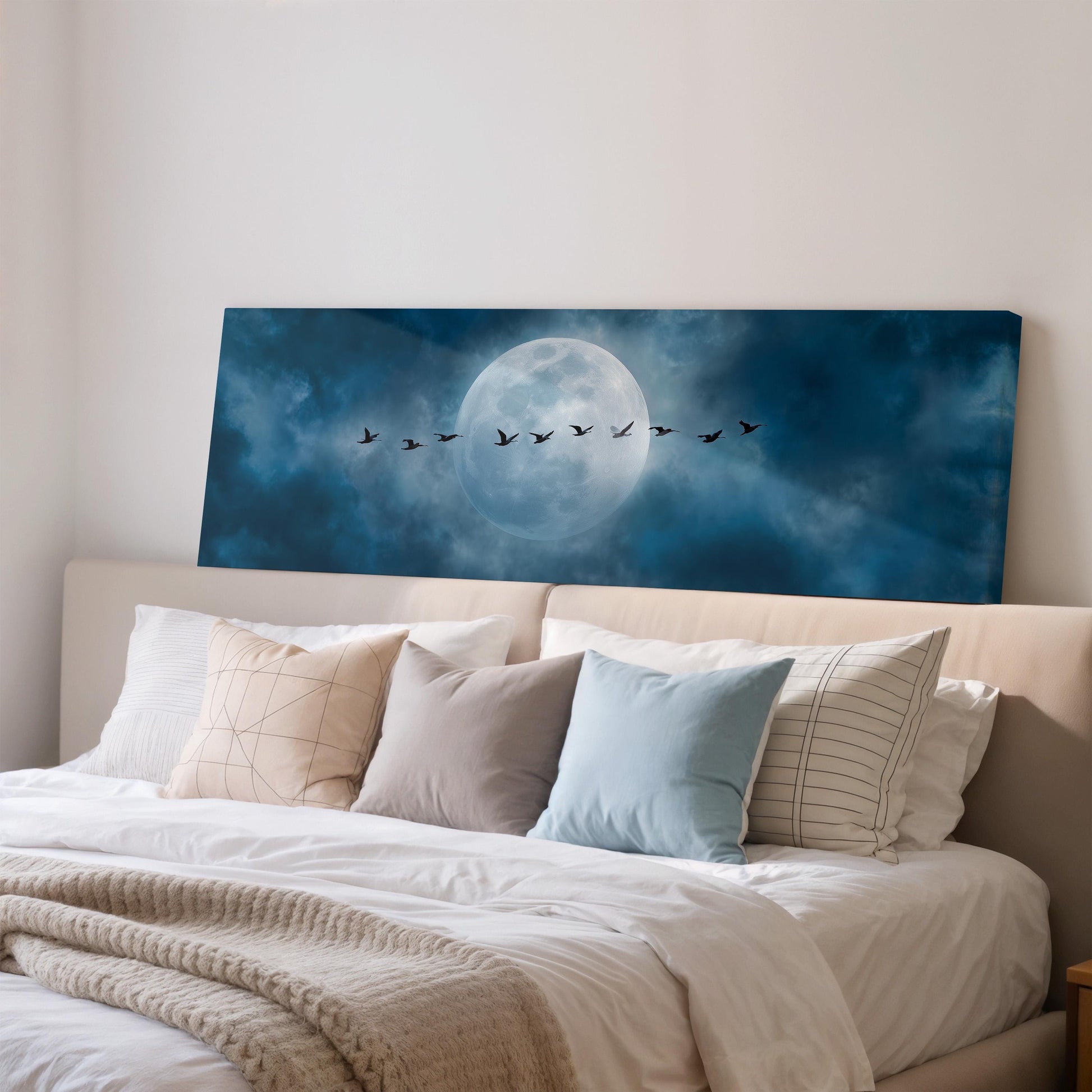 a large bed with white sheets and pillows, and a large canvas print of a night sky with a full moon and a flock of birds flying across it.