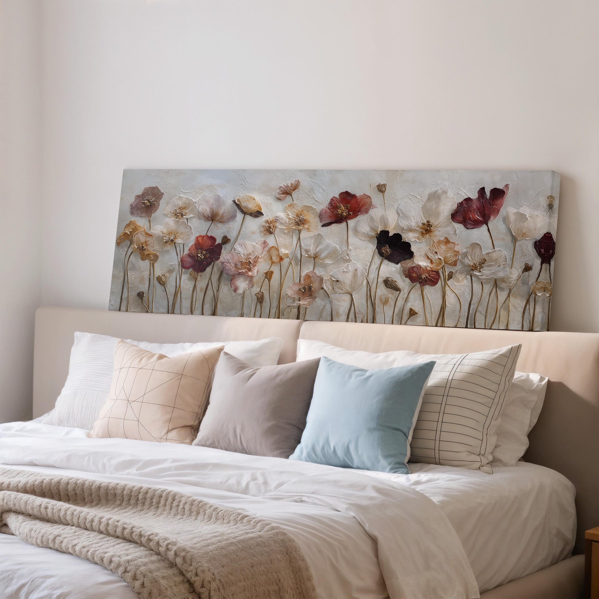 a cozy bedroom with a large bed adorned with white linens and a variety of colorful pillows. Above the bed, there is a large painting of flowers, adding a touch of nature and beauty to the room.