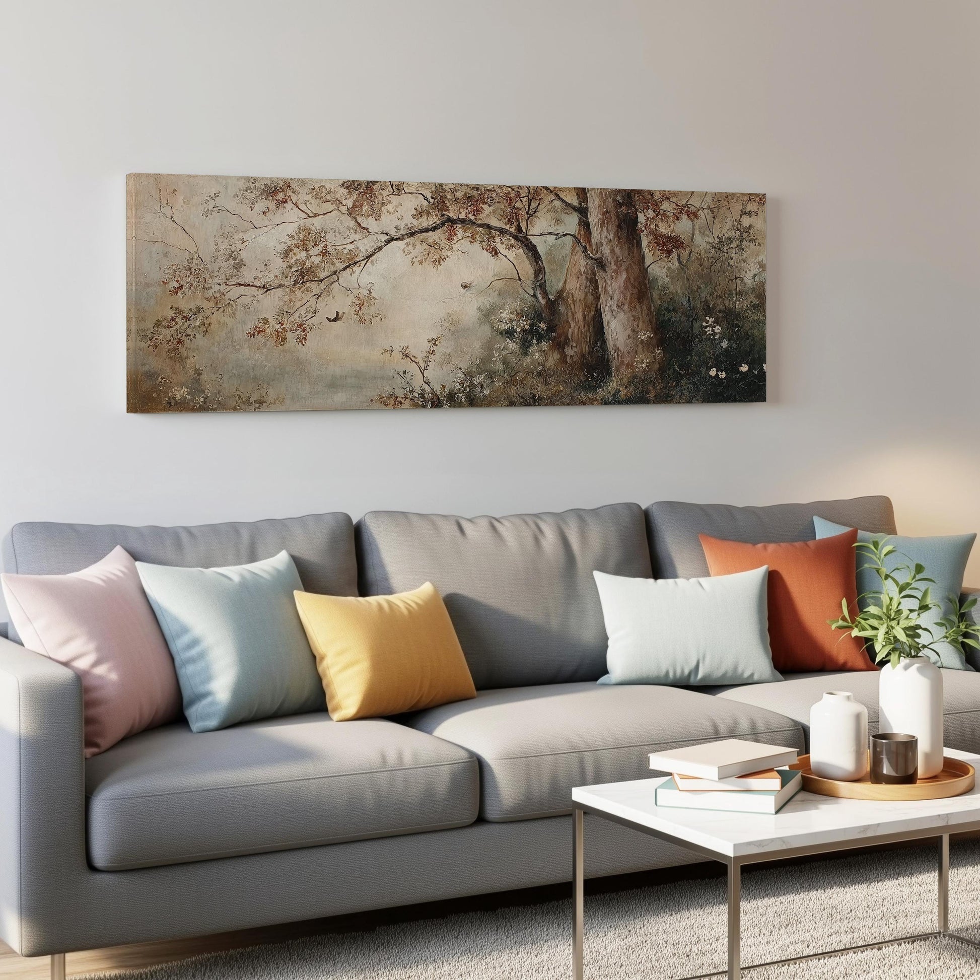 a gray couch with colorful throw pillows, a coffee table with books and a plant, and a large painting of a tree hanging on the wall above the couch.