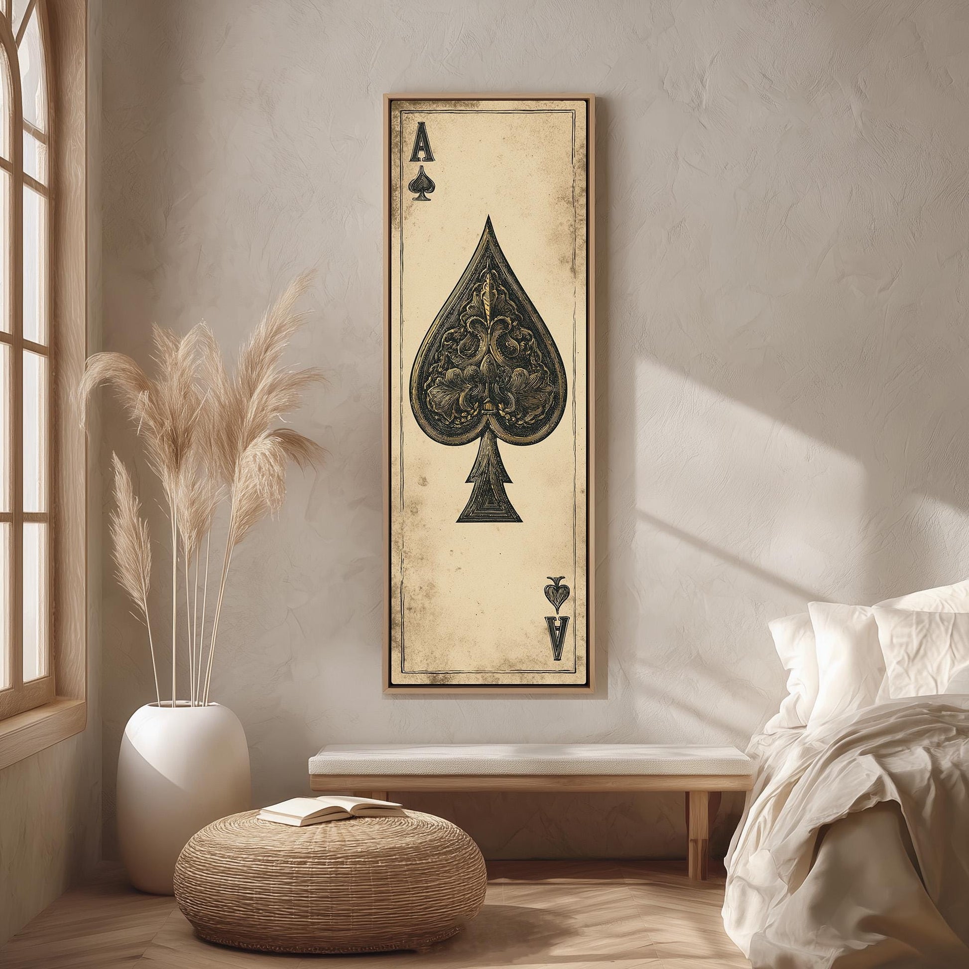 a bedroom setting with a large framed artwork of a spade on the wall, a bed with white bedding, a potted plant, and a woven ottoman.