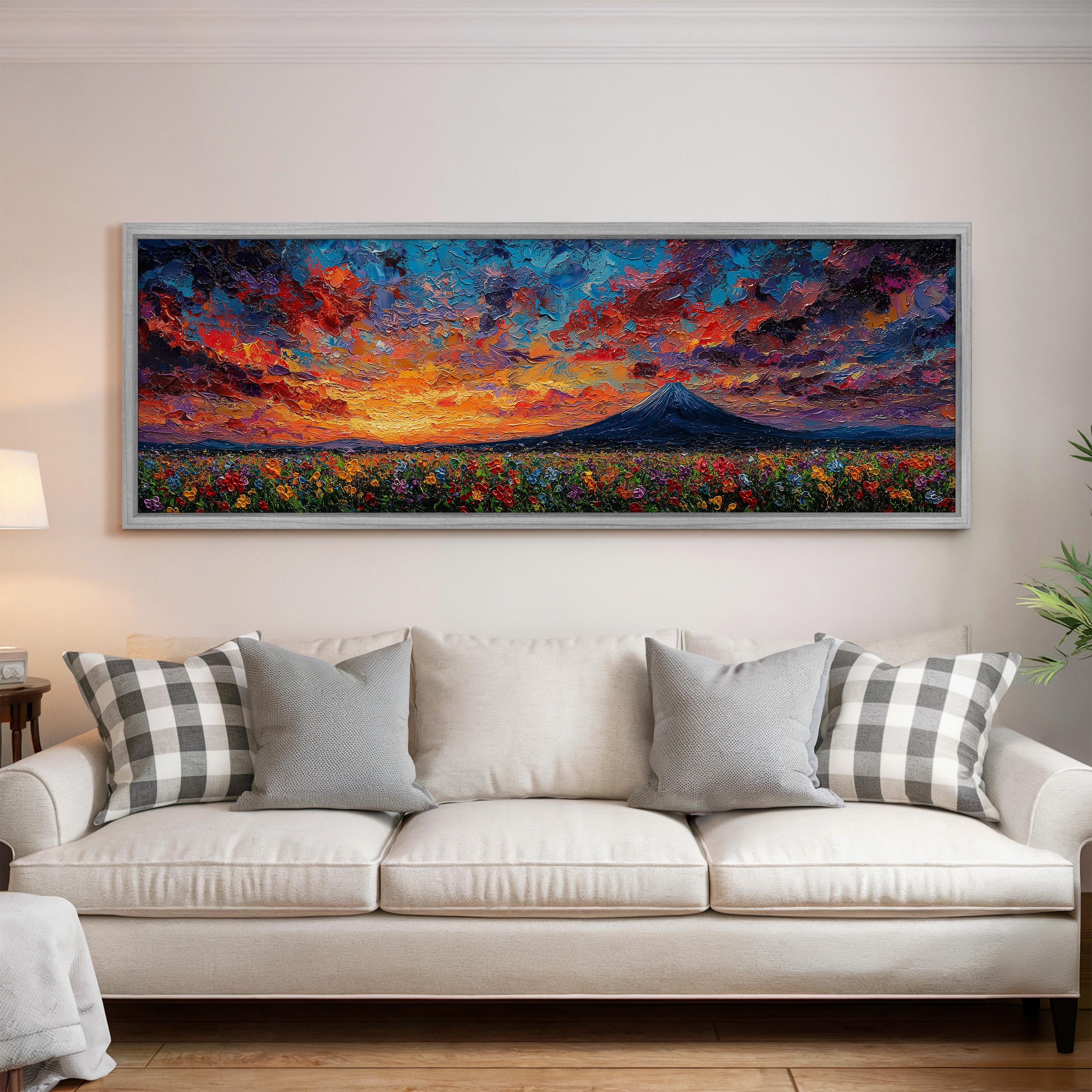a large, colorful painting of a landscape with a mountain and a field of flowers, hanging on a wall above a white couch with gray and white patterned pillows.