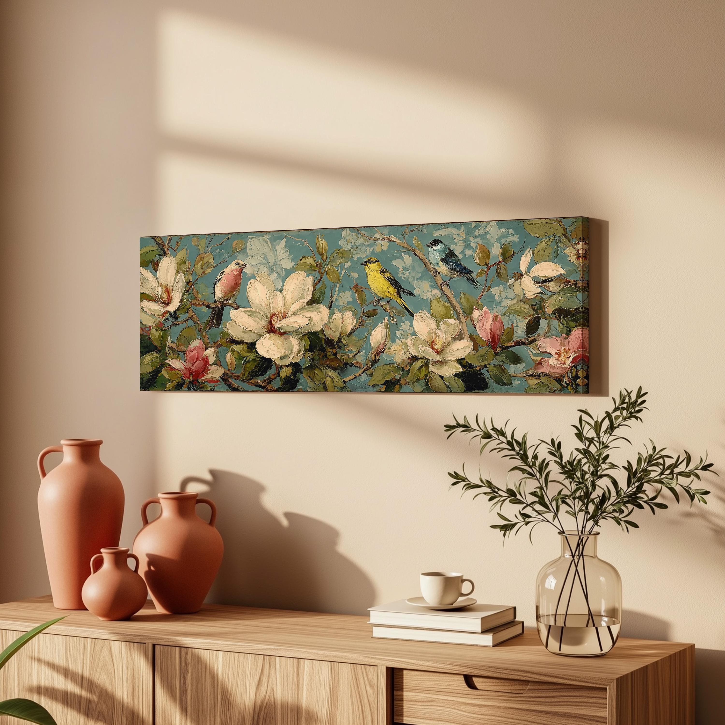 a wooden cabinet with a vase, a coffee cup, and a stack of books on top. Above the cabinet, there is a framed painting of flowers and birds.