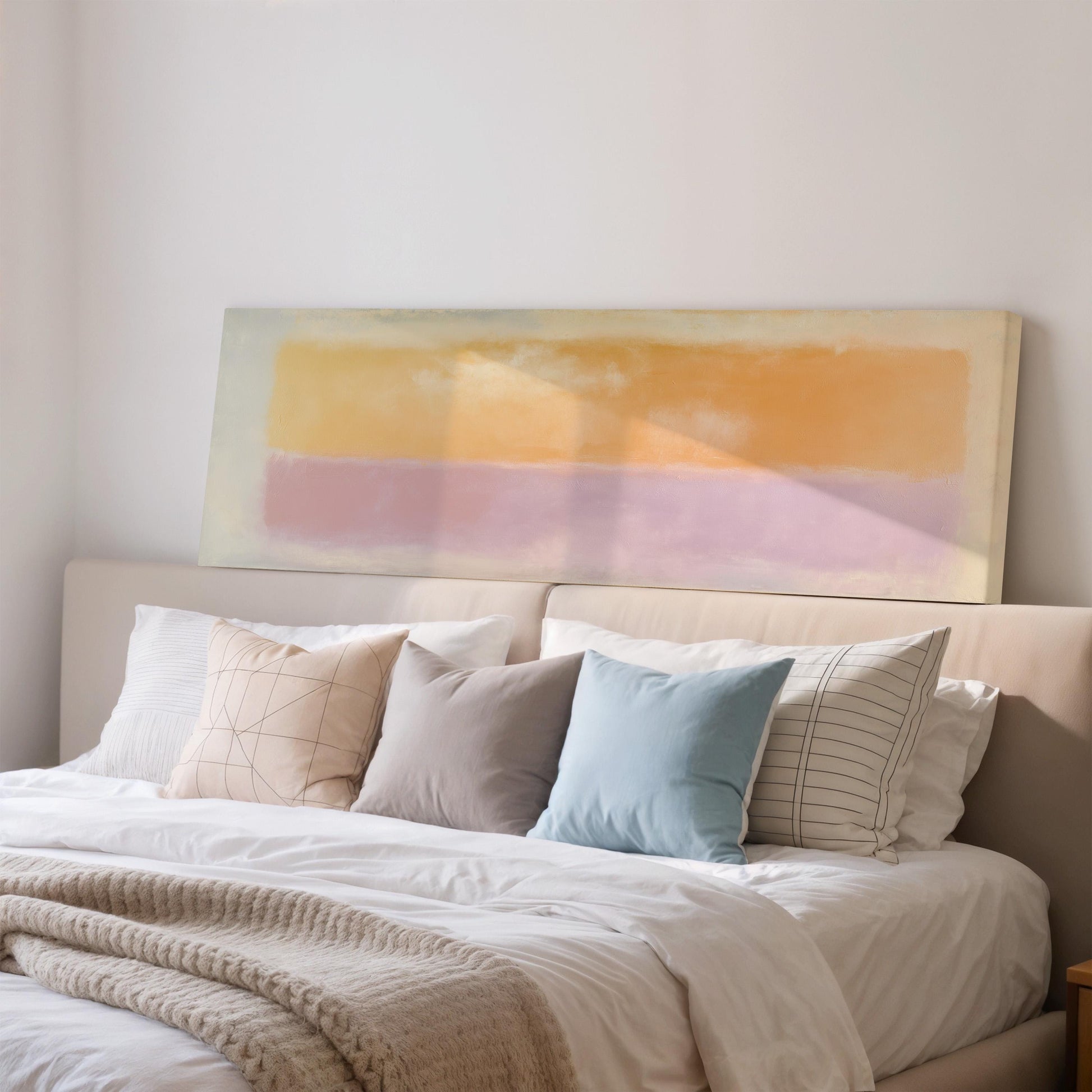 a cozy bedroom with a large bed adorned with a white comforter and a variety of colorful pillows. Above the bed, there is a large abstract painting in shades of yellow, pink, and orange.
