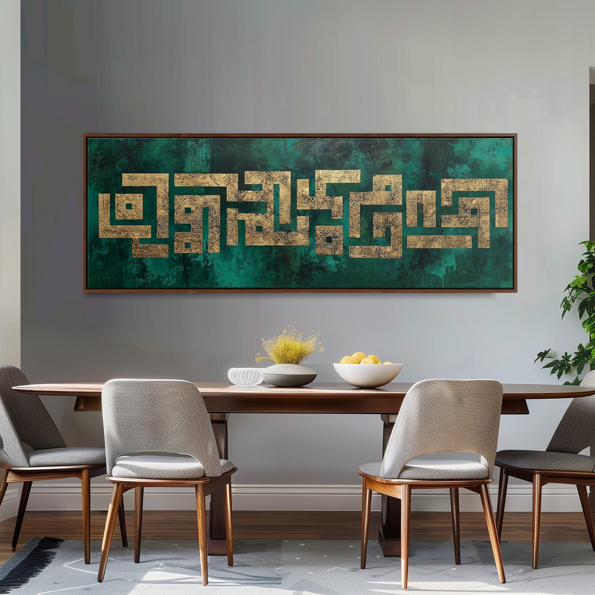 a dining room with a wooden table and four chairs. Above the table, there is a large framed artwork with a green and gold color scheme. The artwork is positioned above a bowl of fruit, which includes apples and oranges. The overall setting appears to be a modern and stylish dining area.