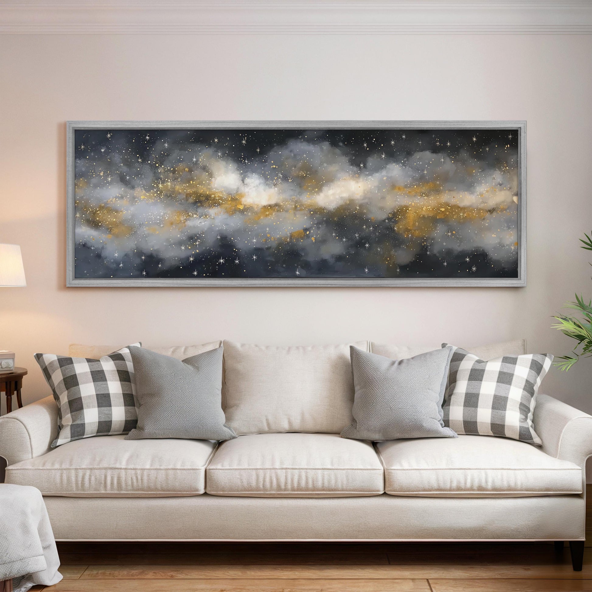 a large, framed painting of a night sky with clouds and stars hanging on a wall above a white sofa with gray and white plaid throw pillows.