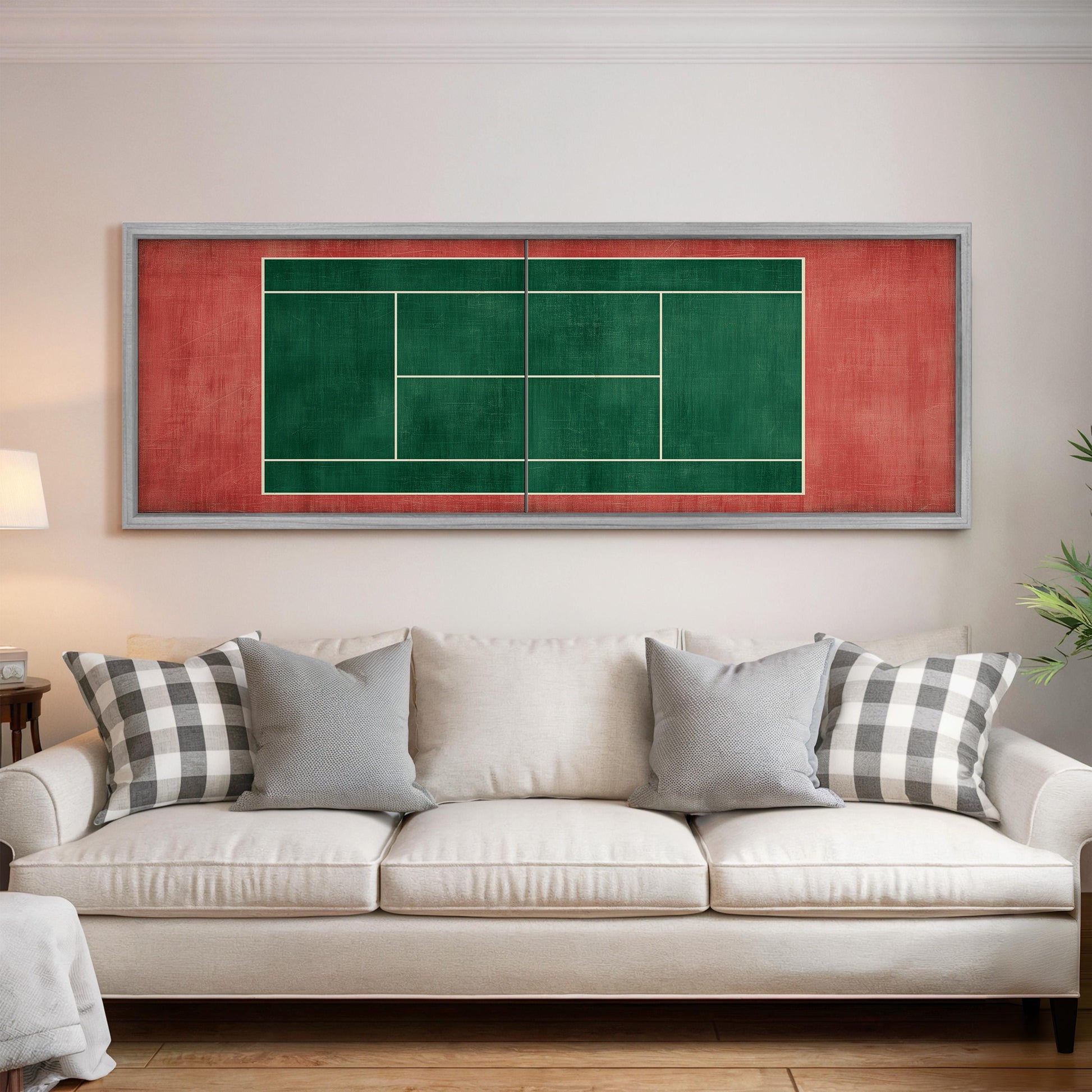 a white couch with gray and black plaid throw pillows, and a framed tennis court with a red and green background is displayed on the wall above the couch.