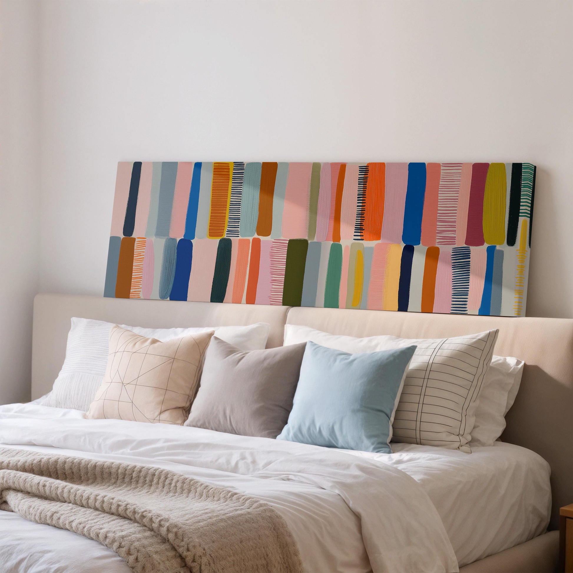 a cozy bedroom scene with a bed adorned with white linens and colorful throw pillows. Above the bed, there is a vibrant abstract painting in shades of pink, blue, green, and orange.