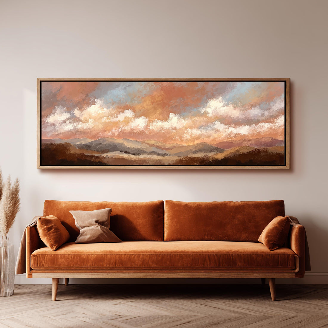 a large, framed painting of a landscape with mountains and clouds hanging on a wall above a brown sofa with pillows.