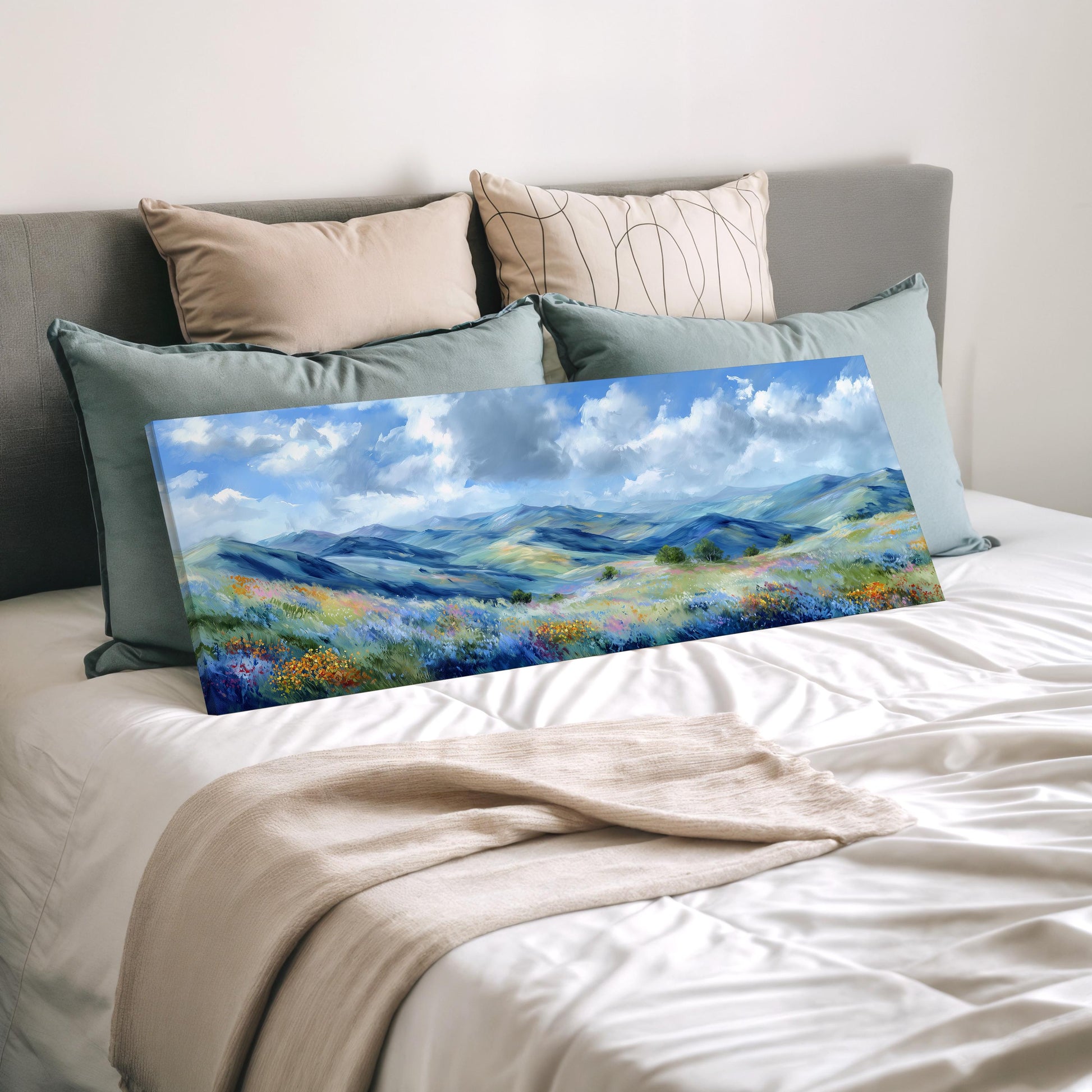 a large landscape painting displayed on a bed, with a beige blanket and pillows surrounding it.