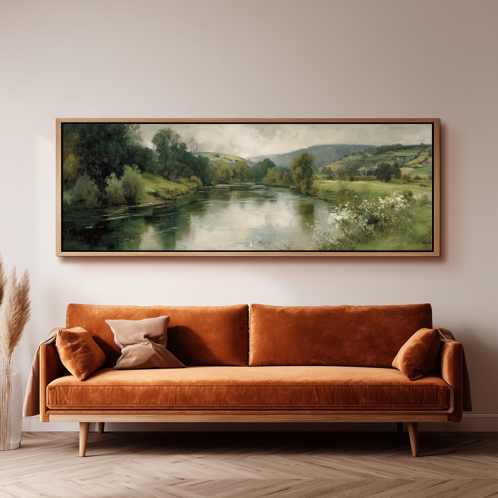 a large painting of a serene landscape hanging on a wall above a brown sofa with orange cushions.