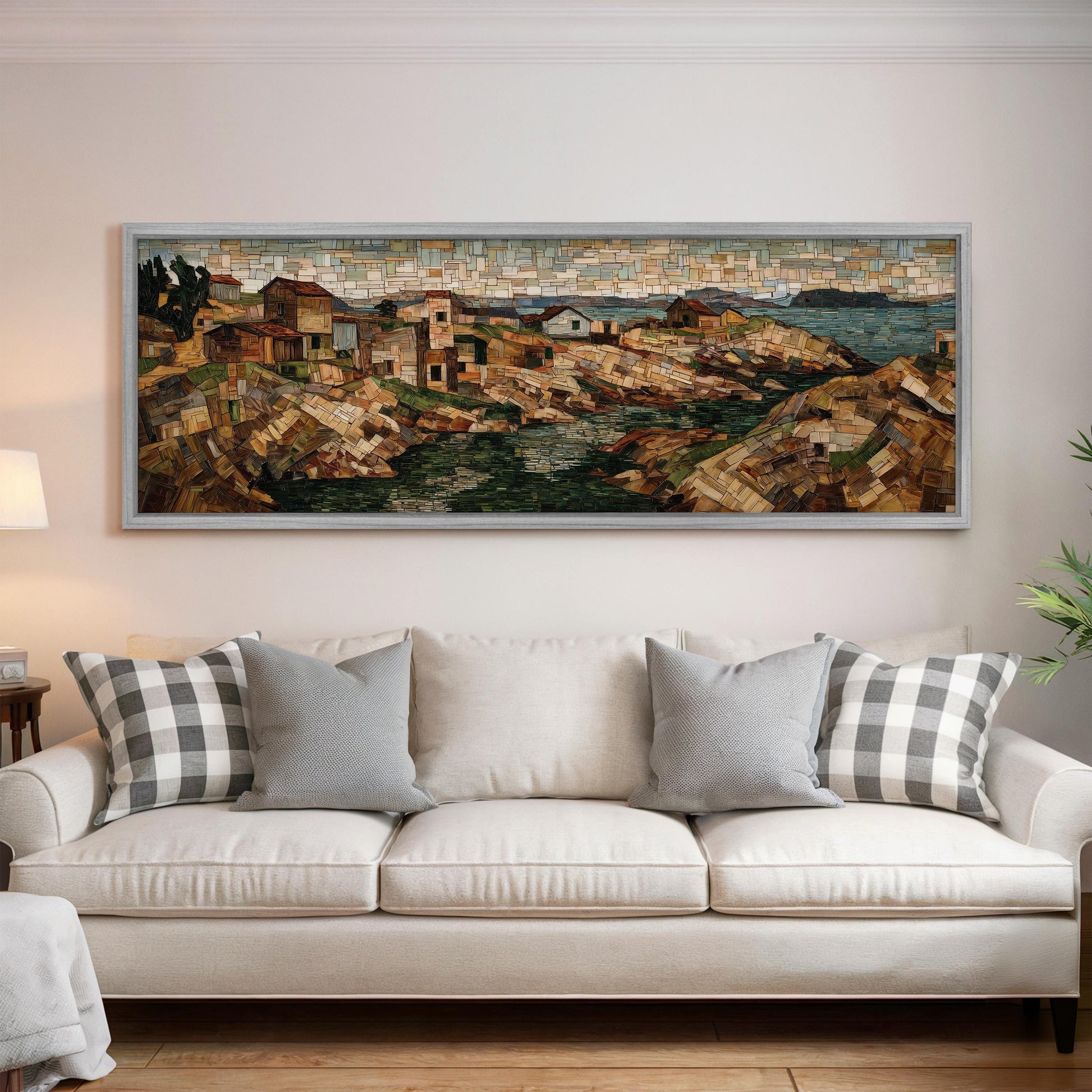 a large, framed painting of a coastal town hanging on a wall above a white couch with gray and white plaid throw pillows.
